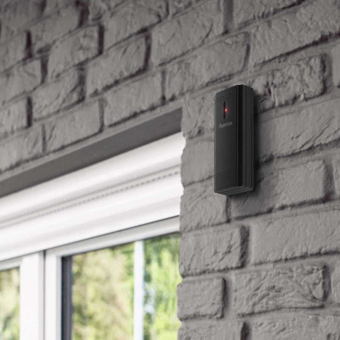 Czarny gong drzwiowy umieszczony na szarej ceglnej ścianie wewnątrz budynku, powyżej okna.