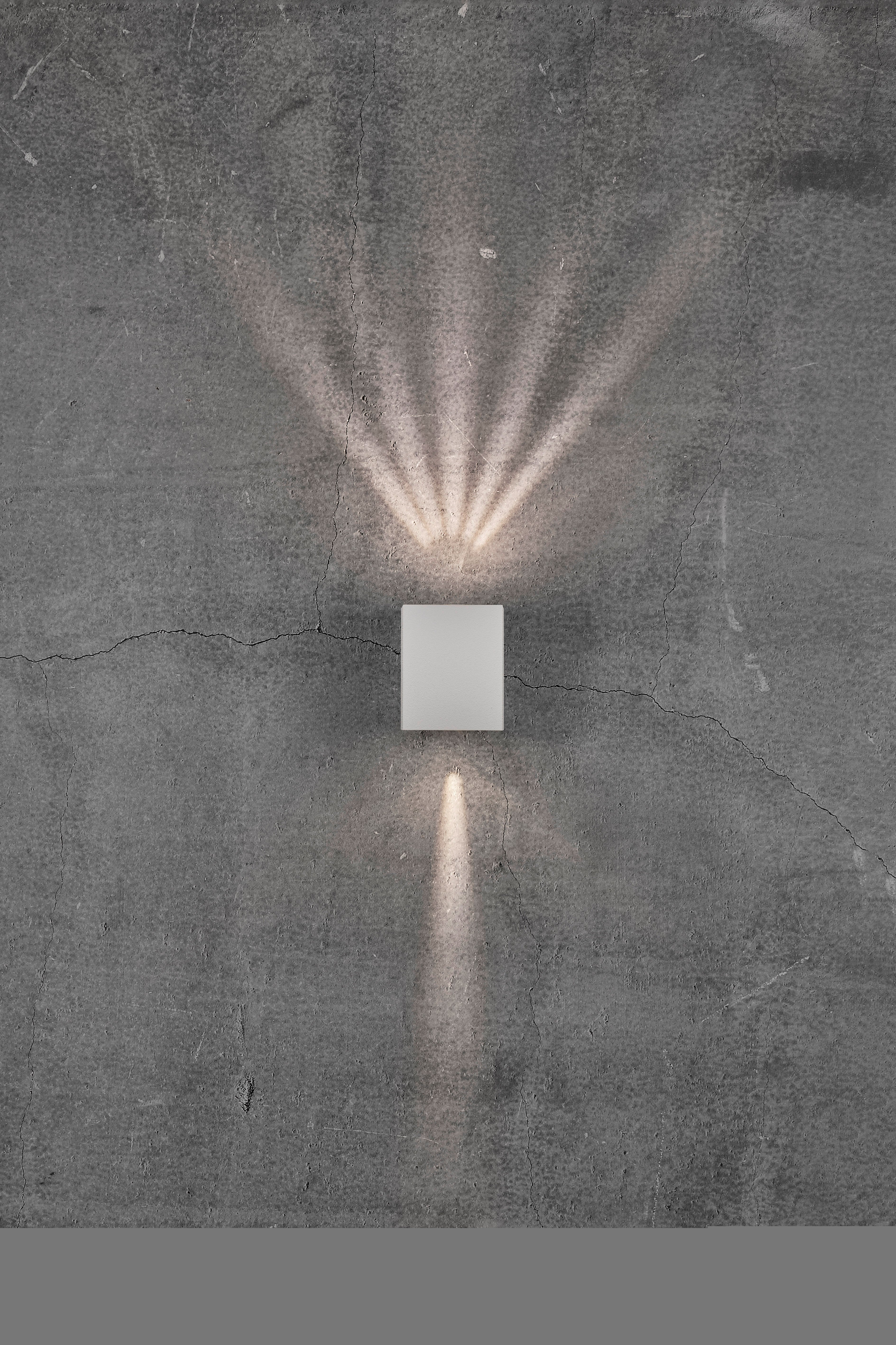 Kinkiet na szarej betonowej ścianie rzuca smugi światła w górę i w dół, tworząc dekoracyjny wzór.