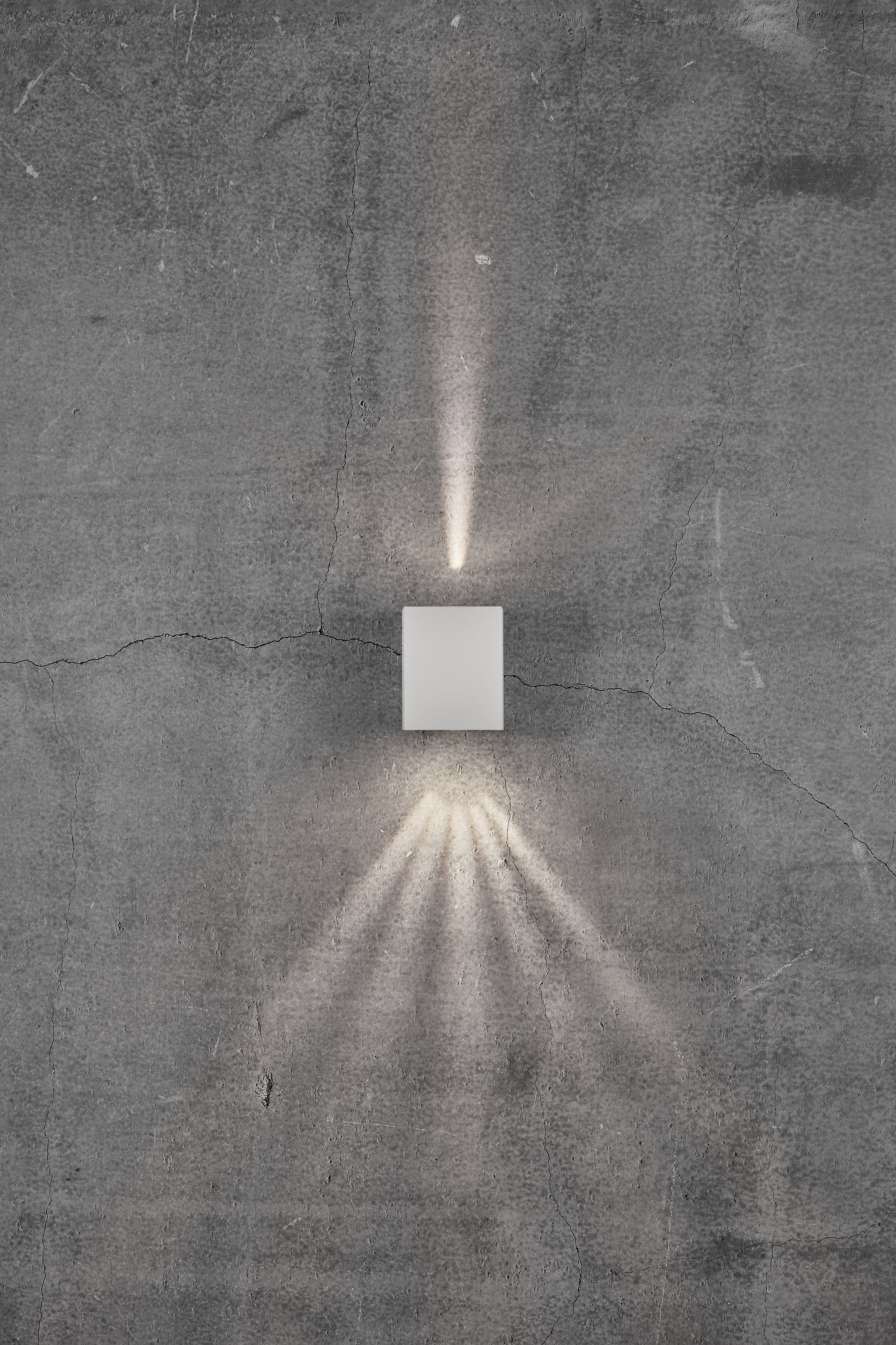 Kinkiet na ścianie betonowej zapewnia równomierne, pośrednie oświetlenie skierowane w górę i w dół.