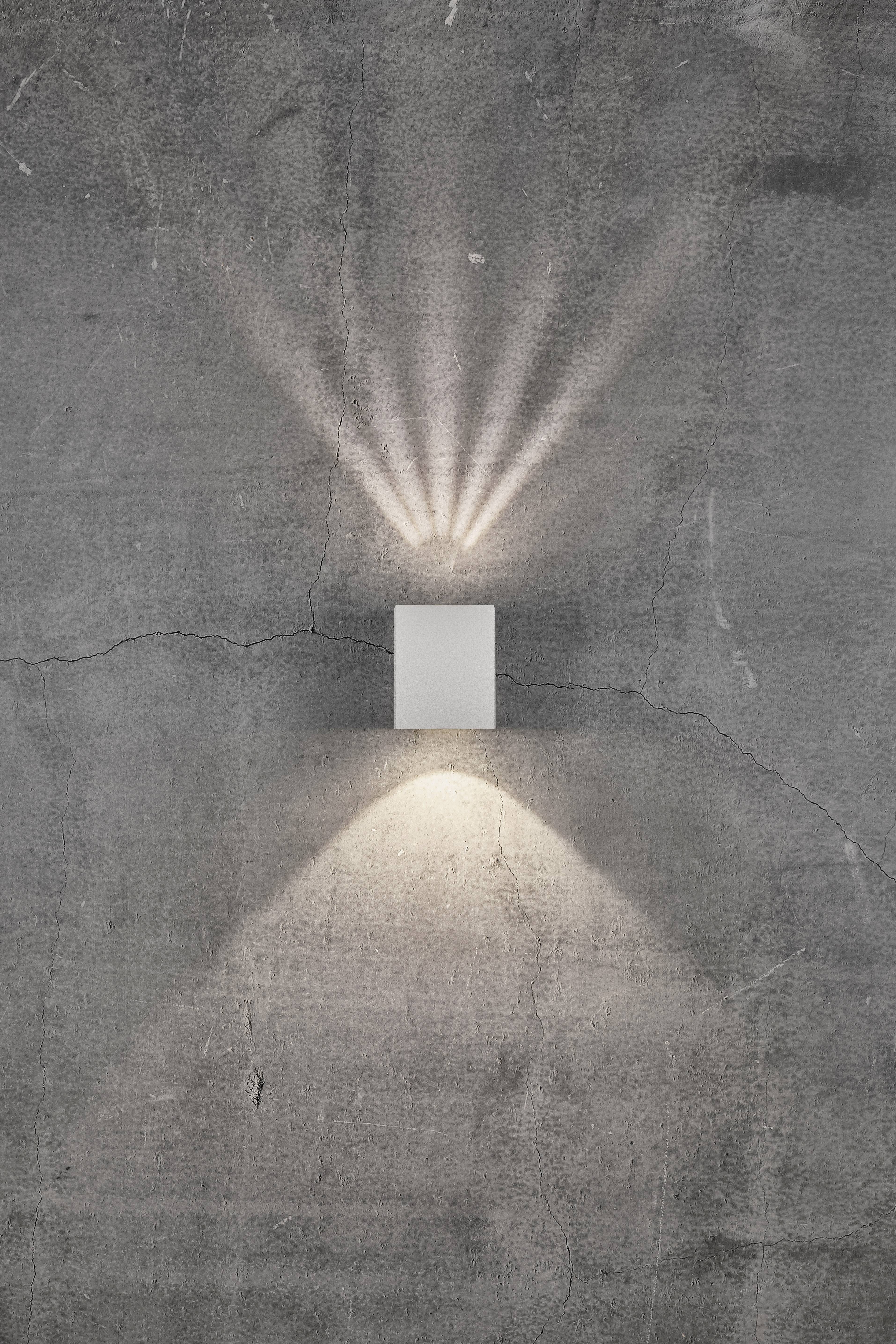 Kinkiet na szarej ścianie betonowej, emitujący promienie skierowane w górę i miękkie światło rozpraszające się w dół, nowoczesne oświetlenie.