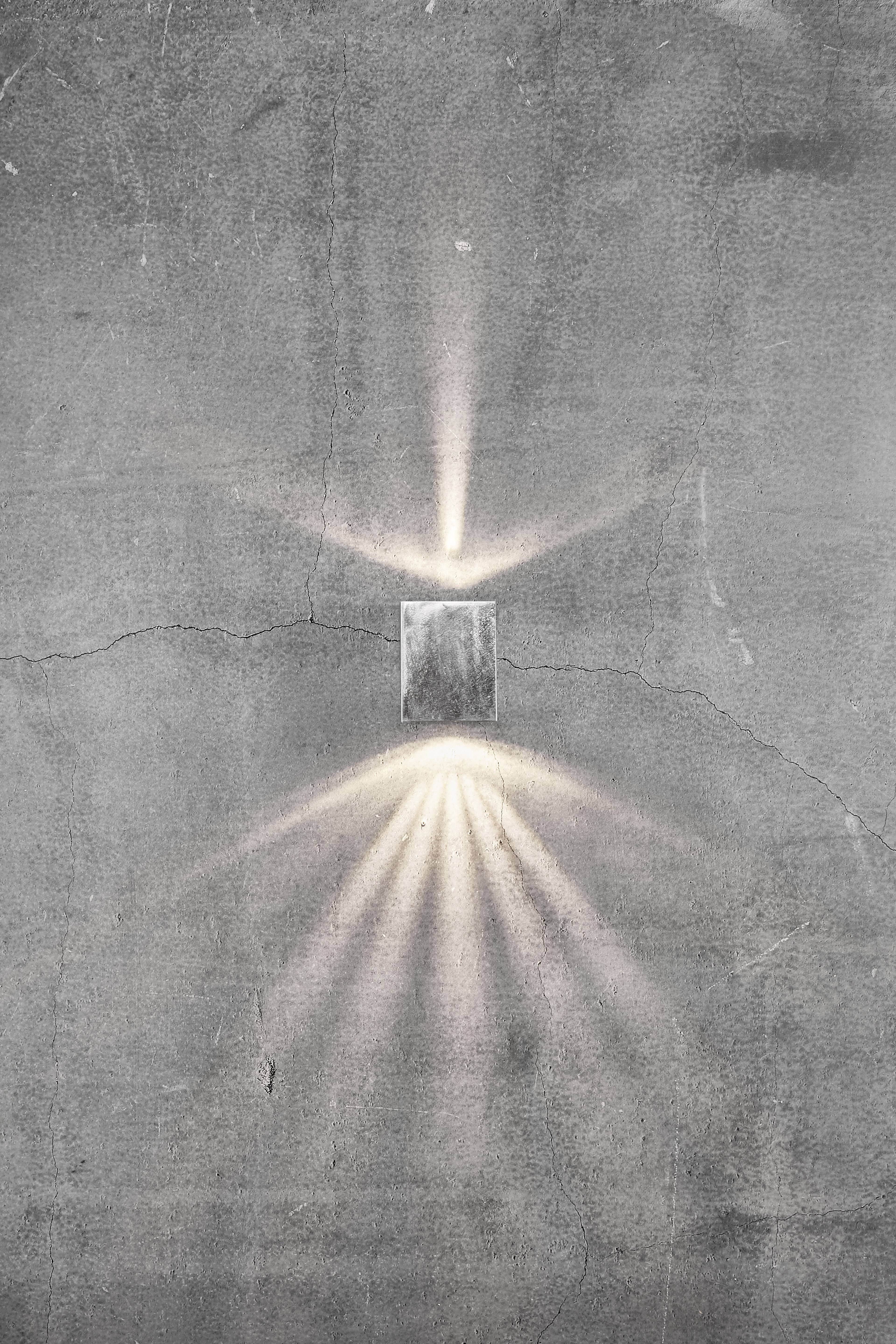 Kinkiet na betonowej ścianie rzuca symetryczne smugi światła, tworząc świetliste wzory i poprawiając oświetlenie pomieszczenia.