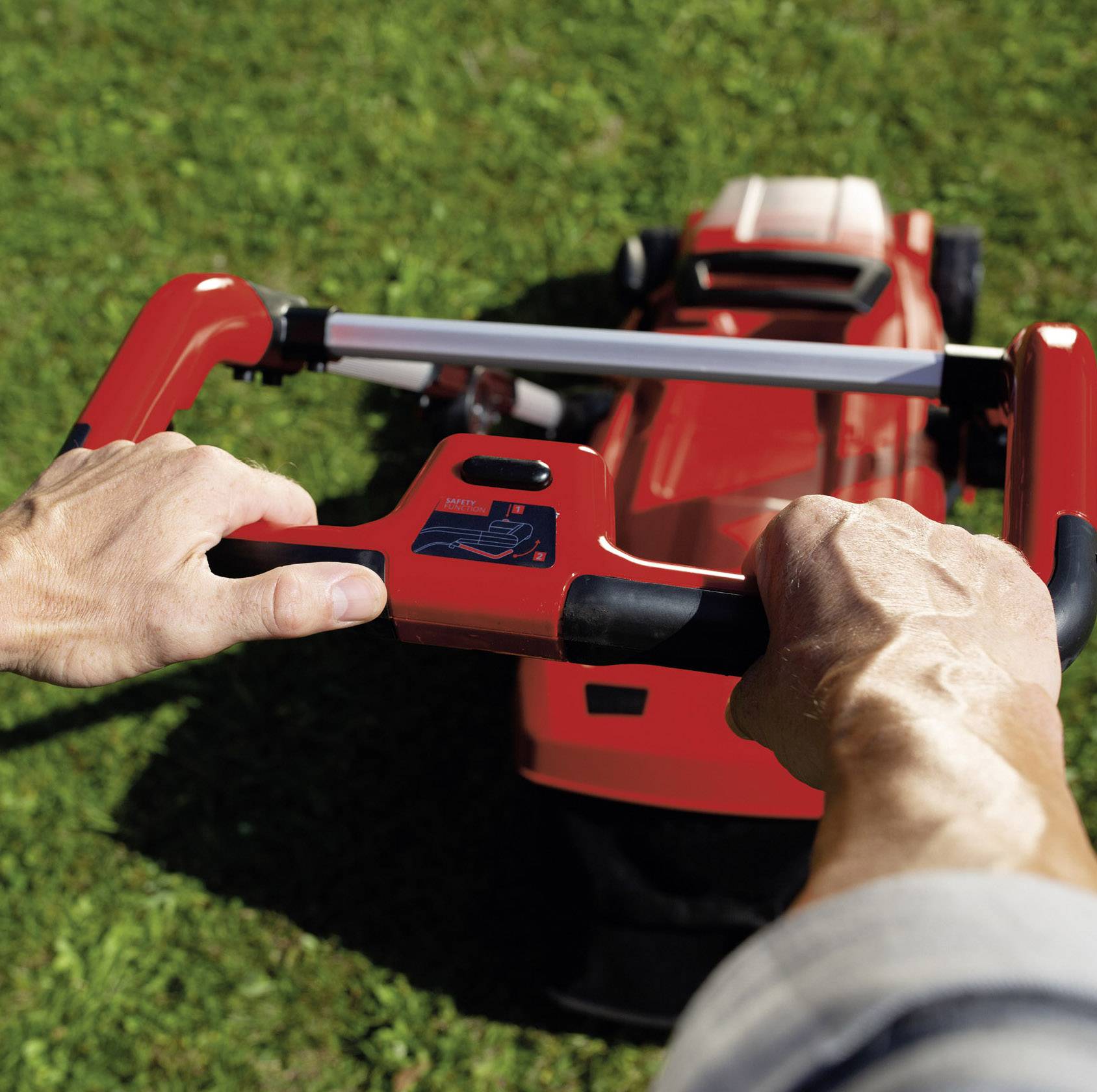 Dwie ręce prowadzą czerwoną kosiarkę przez soczyście zielony trawnik, z fokusem na uchwycie kosiarki.