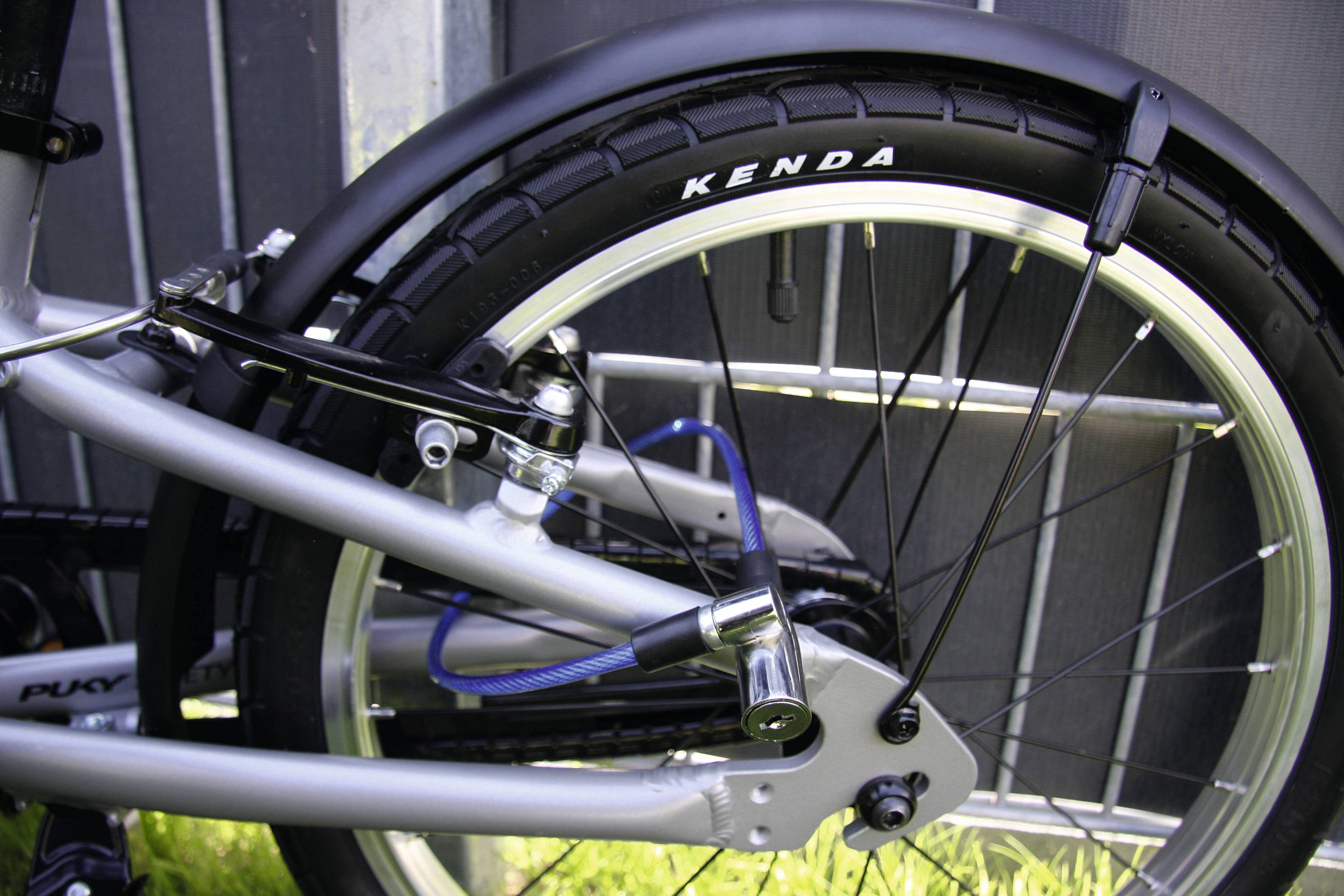 Tylne koło roweru z zamkiem i oponą Kenda, opartego o płot.