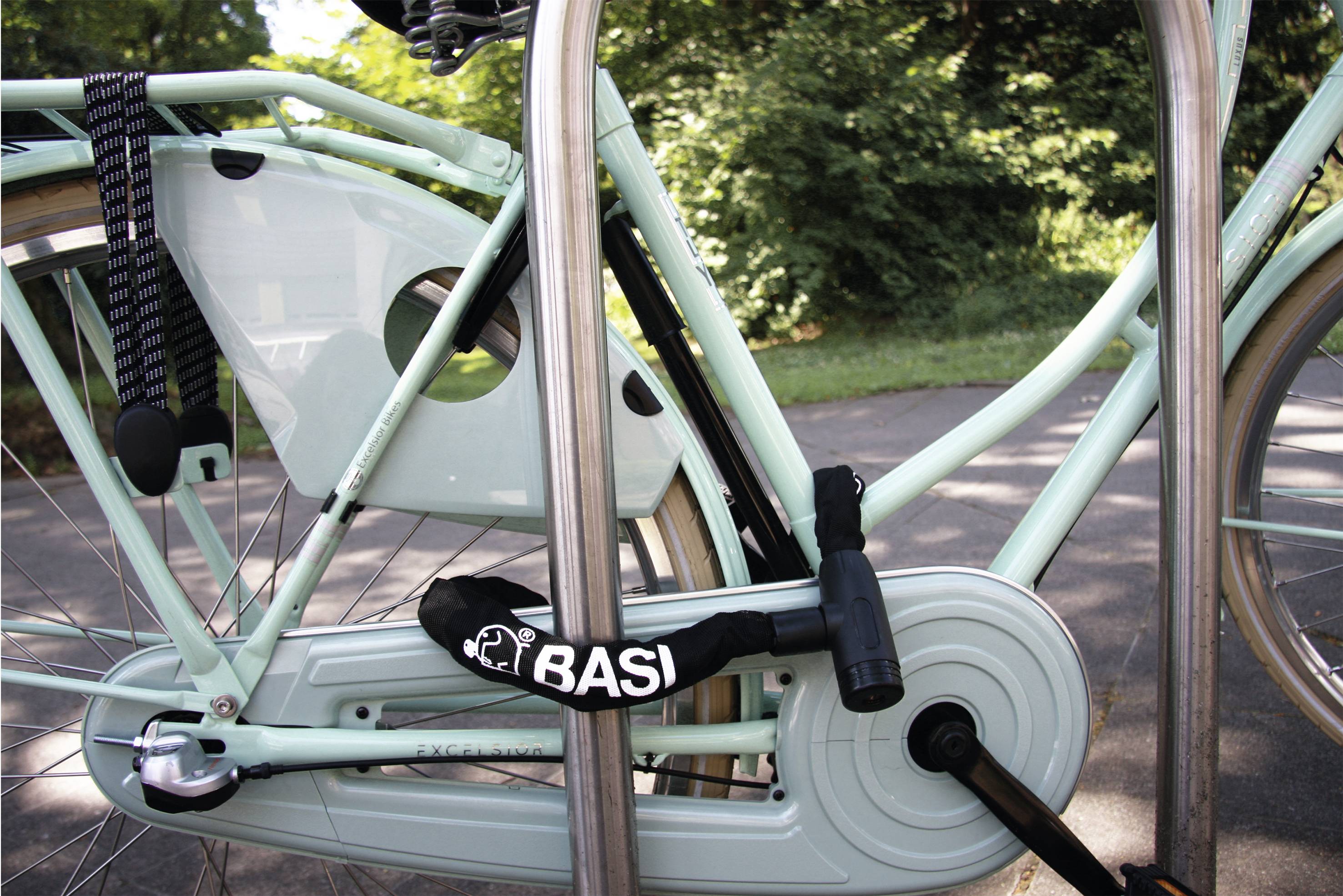 Jasnoniebieskie rower jest zabezpieczony zapięciem rowerowym przy metalowym stojaku, w tle widać drzewa.