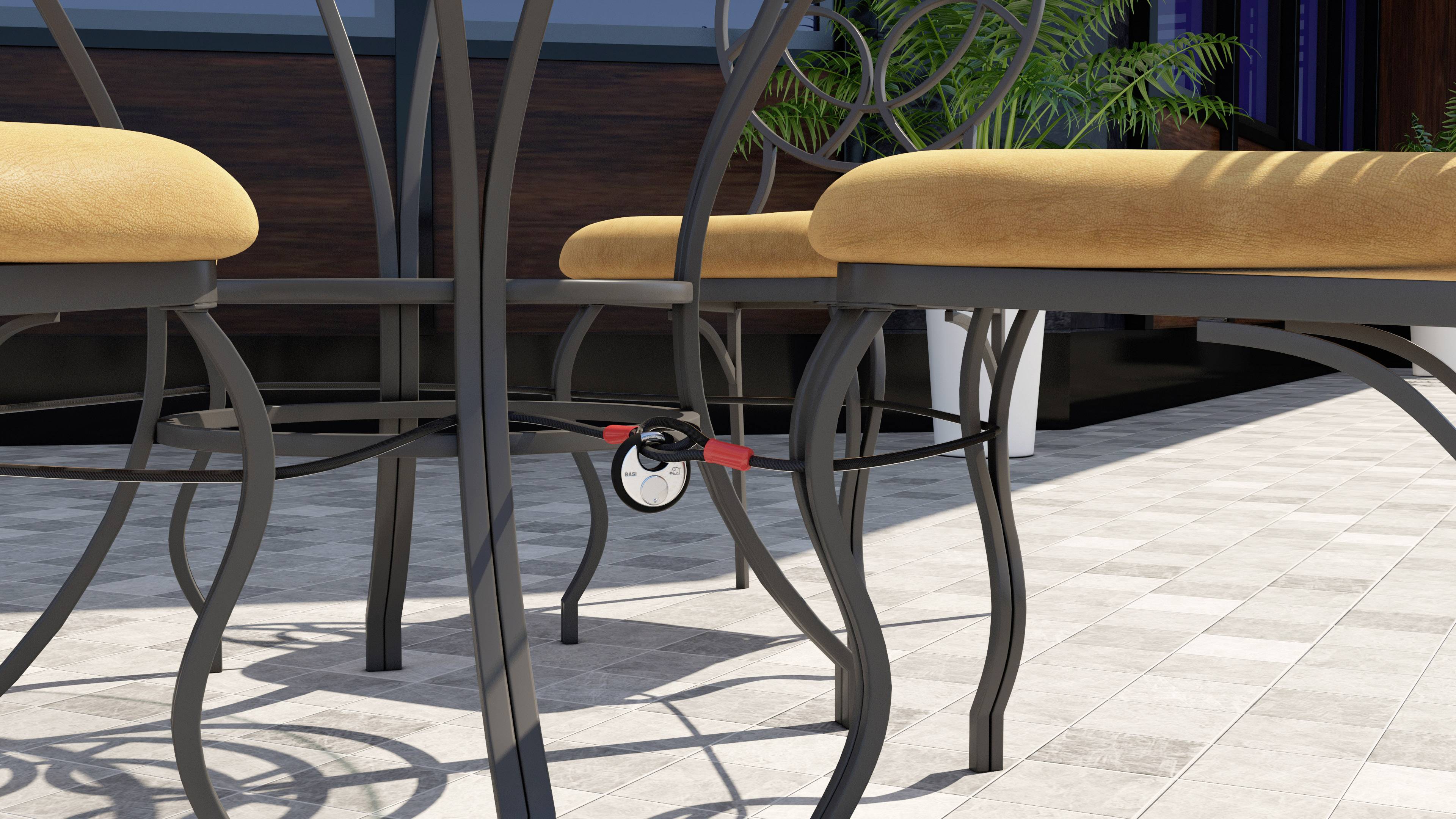 Czerwony rowerowy zamek zabezpiecza dwa czarne metalowe krzesła na tarasie. W tle widać rośliny.