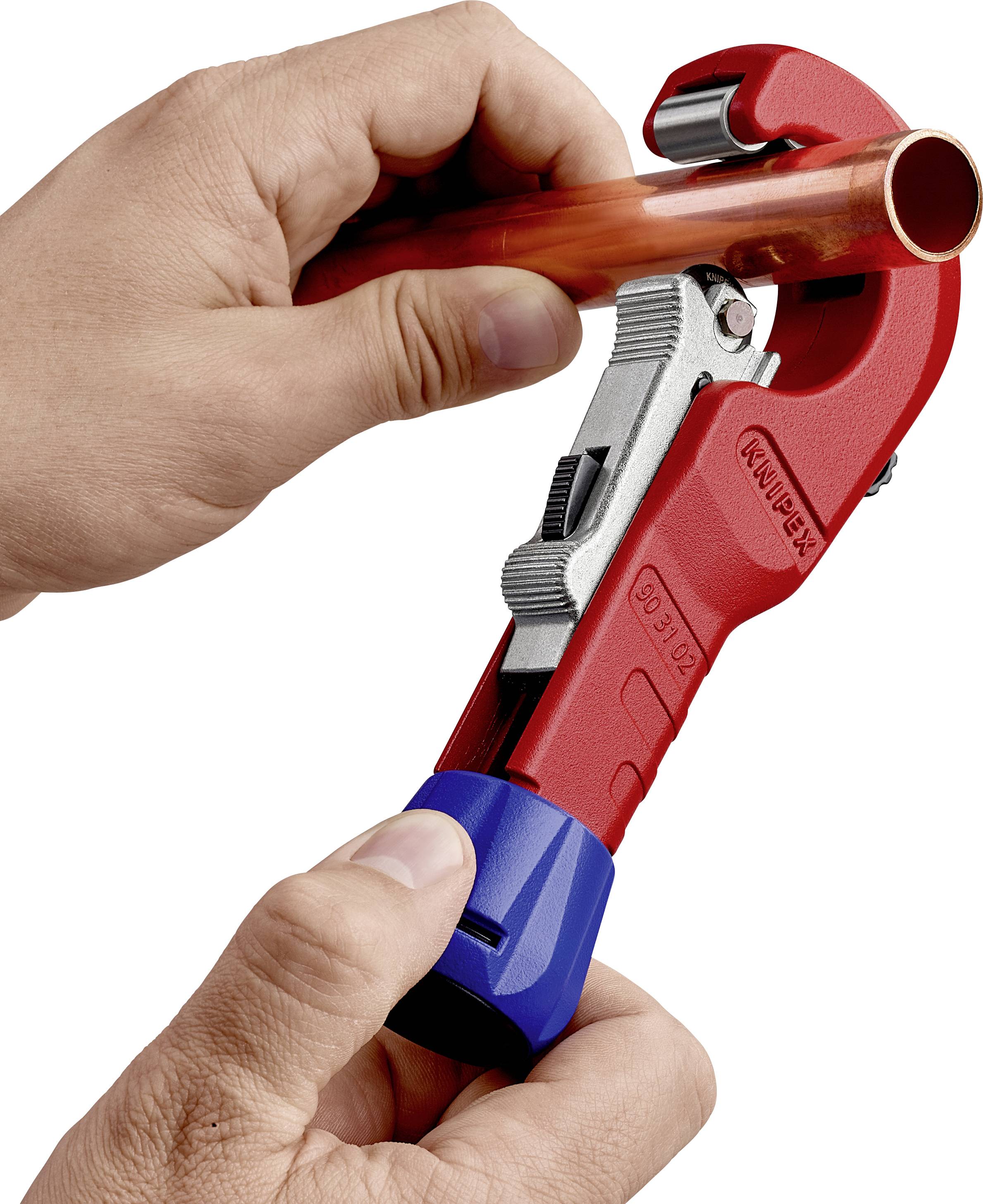 Ręka trzyma obcinacz do rur i przycina miedzianą rurę. Narzędzie jest czerwone z niebieskim uchwytem.