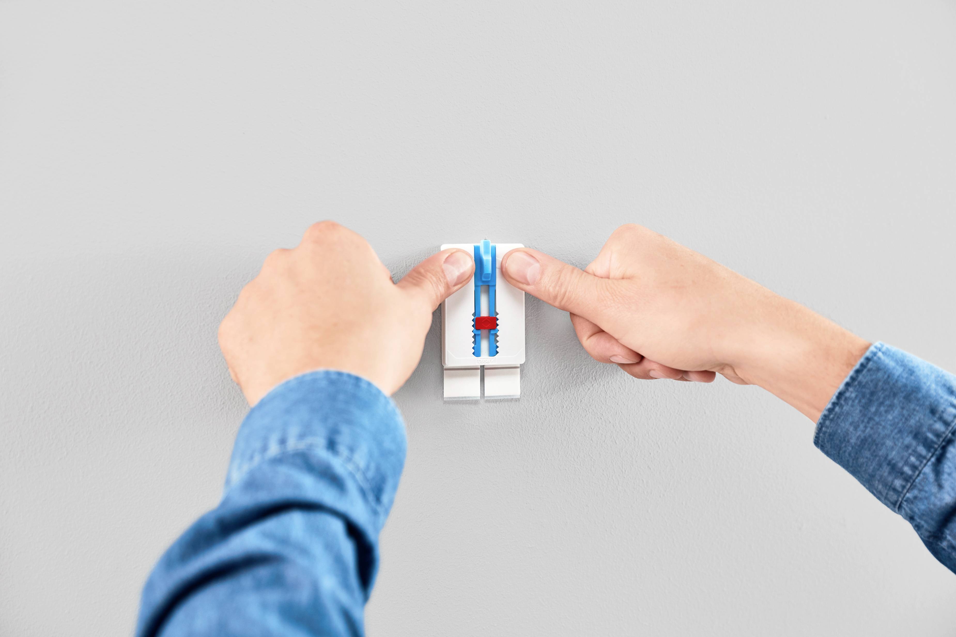 Dwie ręce naciskają przełącznik na gładkiej, jasnoszarej ścianie.