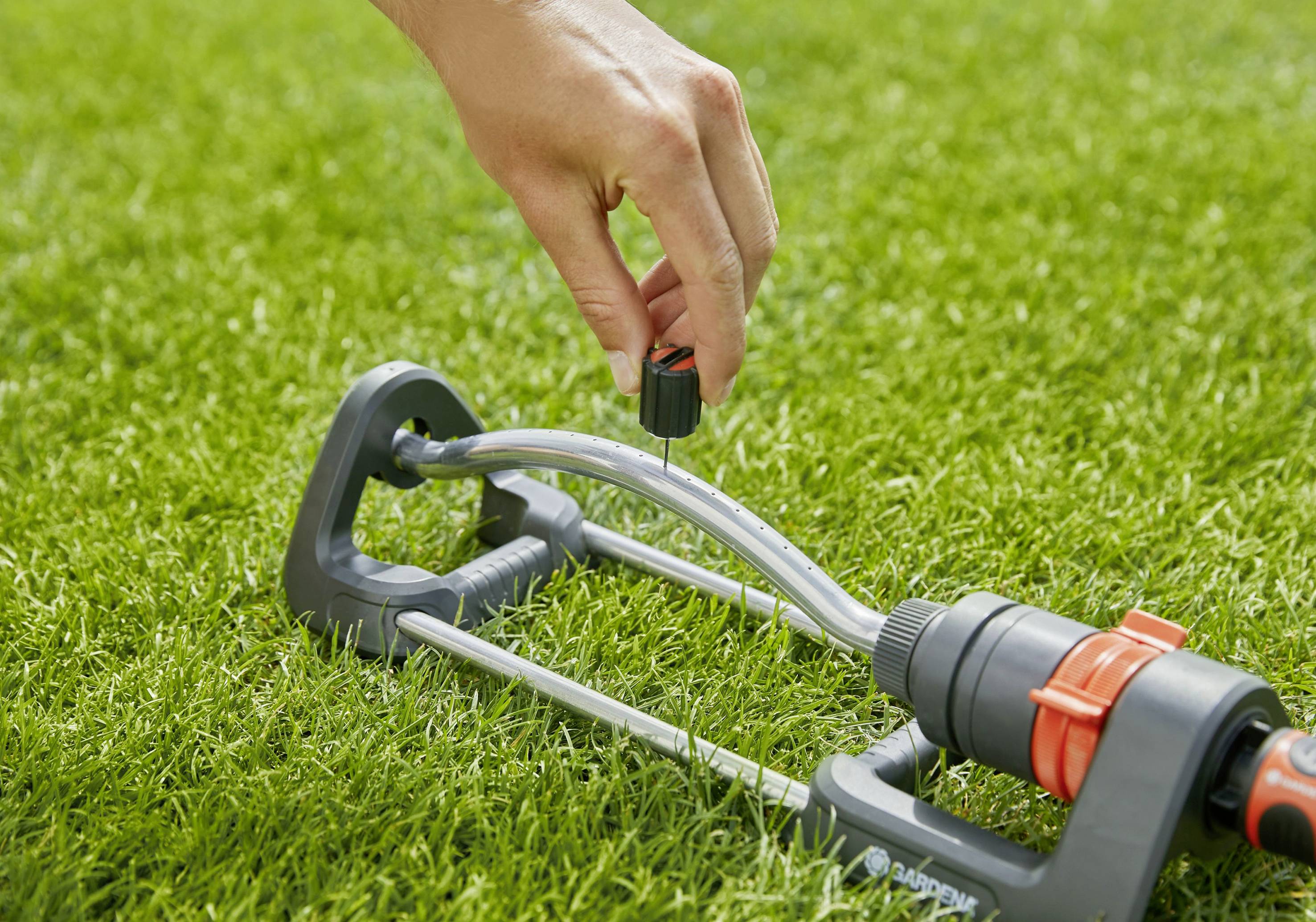 Dłoń reguluje zraszacz na zielonej trawie.