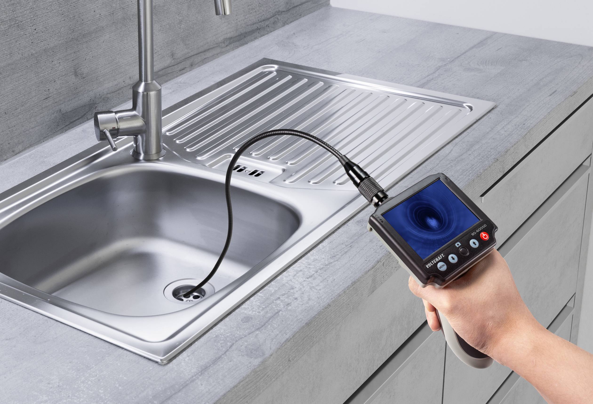 Rzemieślnik sprawdza odpływ zlewki kuchennej za pomocą endoskopu, który wyświetla obraz z rury kanalizacyjnej na ekranie.