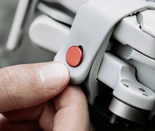 Dłoń naciska czerwony przycisk na białym urządzeniu technicznym.