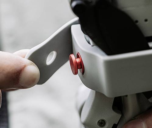 Jedna ręka trzyma szary dźwignik, przymocowany czerwoną śrubą.