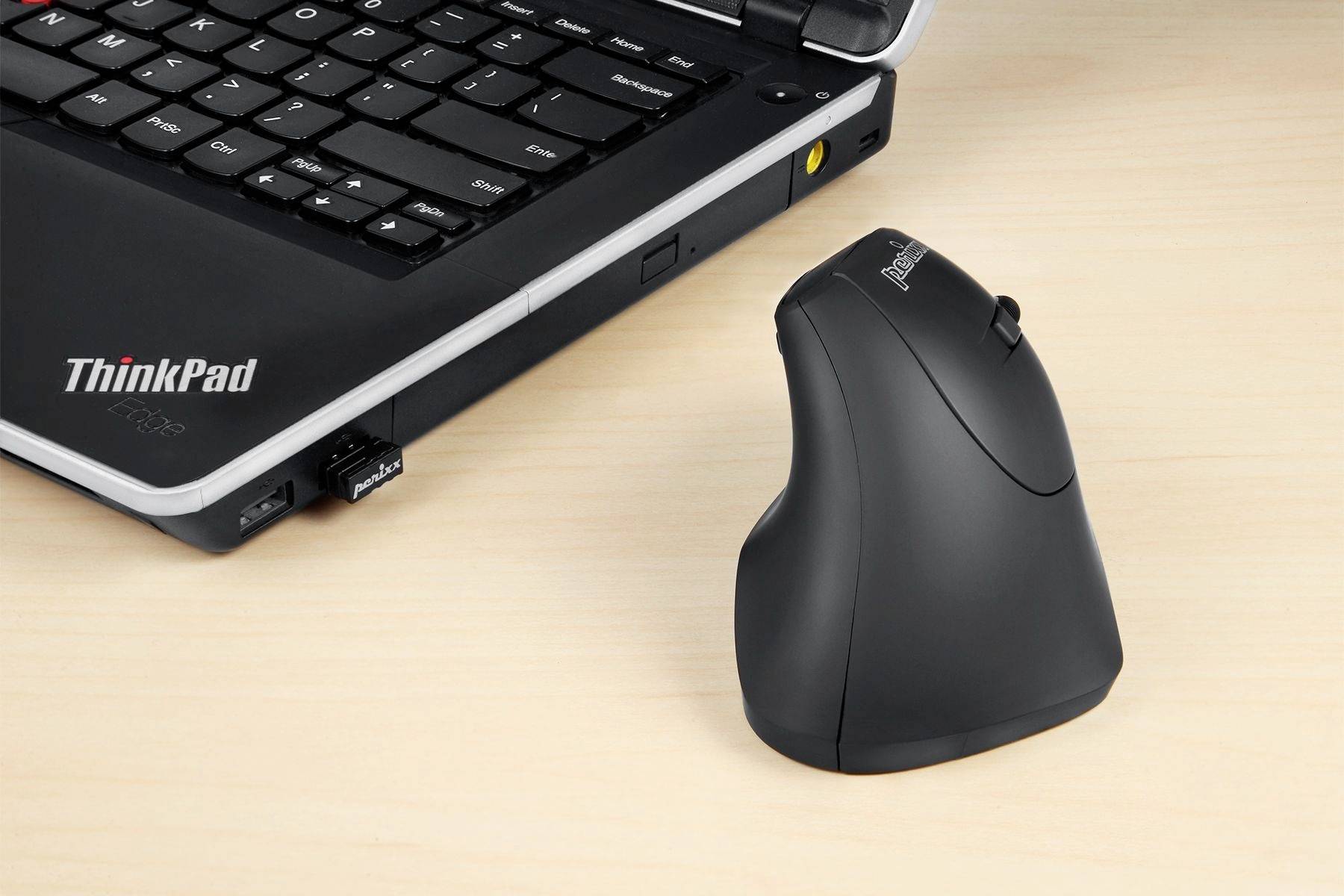 Czarna, ergonomiczna mysz komputerowa obok rozłożonego laptopa na drewnianym stole. Laptop ukazuje częściowo widoczną klawiaturę.