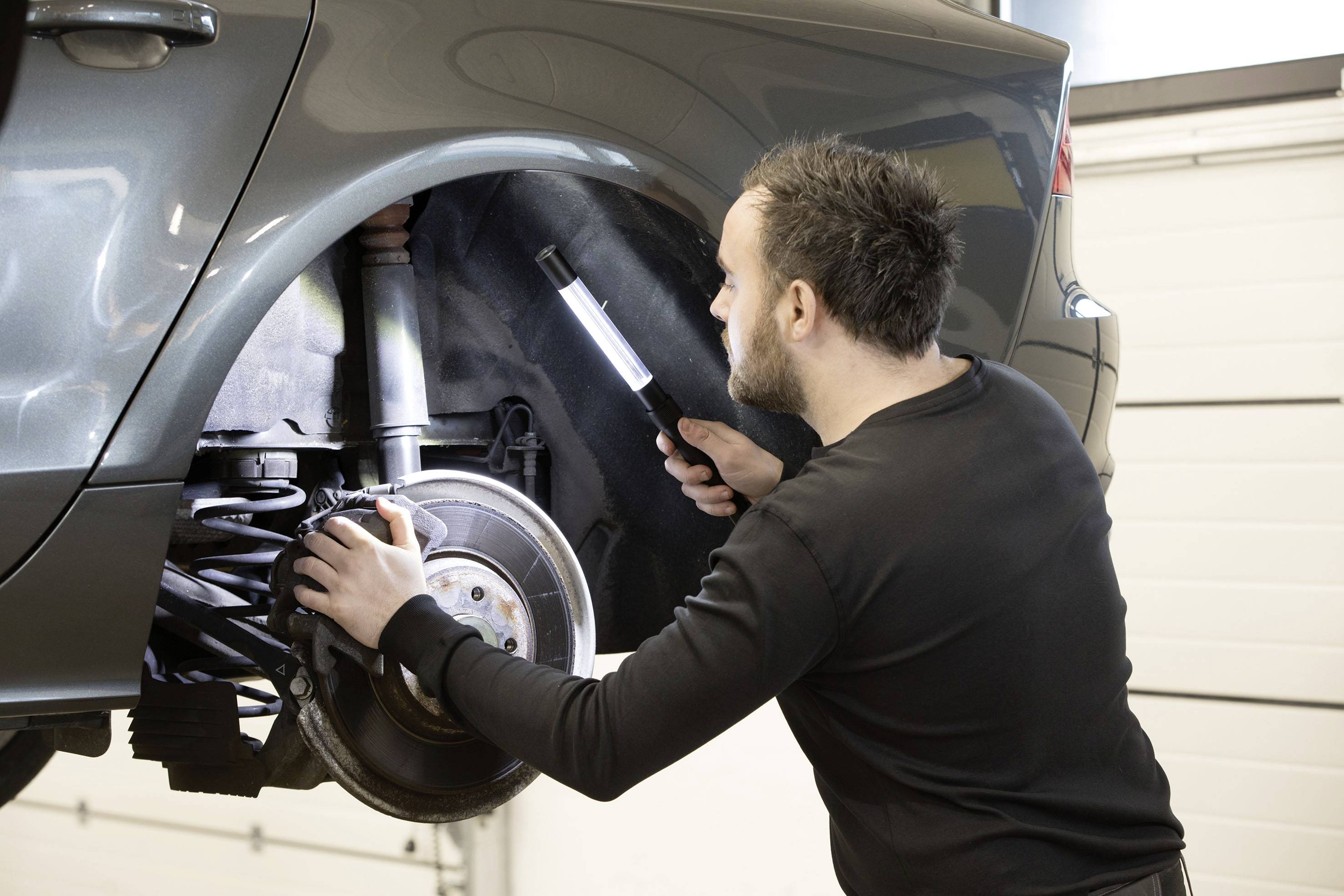 Mechanik sprawdza zawieszenie podniesionego samochodu w warsztacie, trzymając latarkę dla lepszej widoczności.