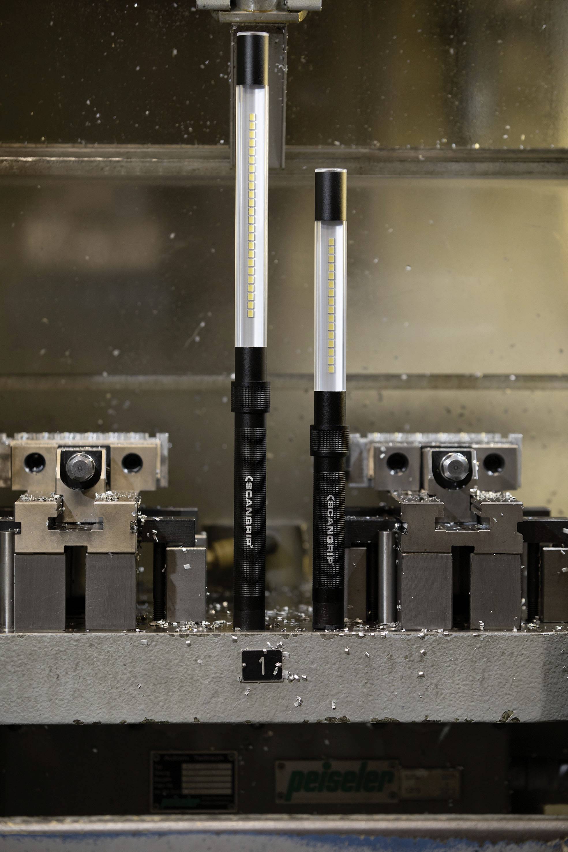 Dwie lampy LED o różnych rozmiarach stoją w otoczeniu przemysłowym na metalowej platformie pomiędzy imadłami.