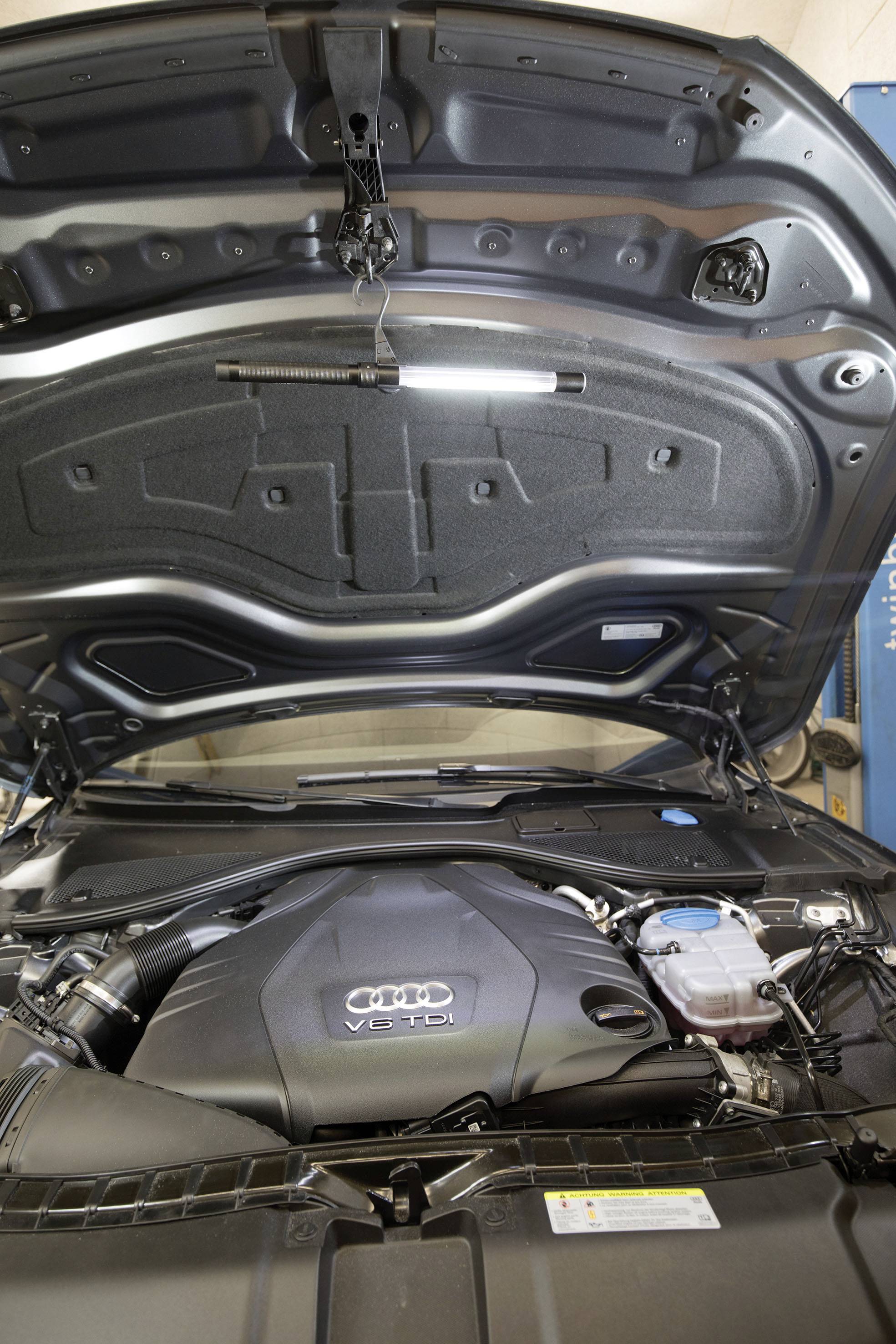 Samochód z otwartą maską prezentuje komorę silnikową Audi. Widoczny jest silnik 'V6 TDI', otoczony różnymi przewodami i elementami.