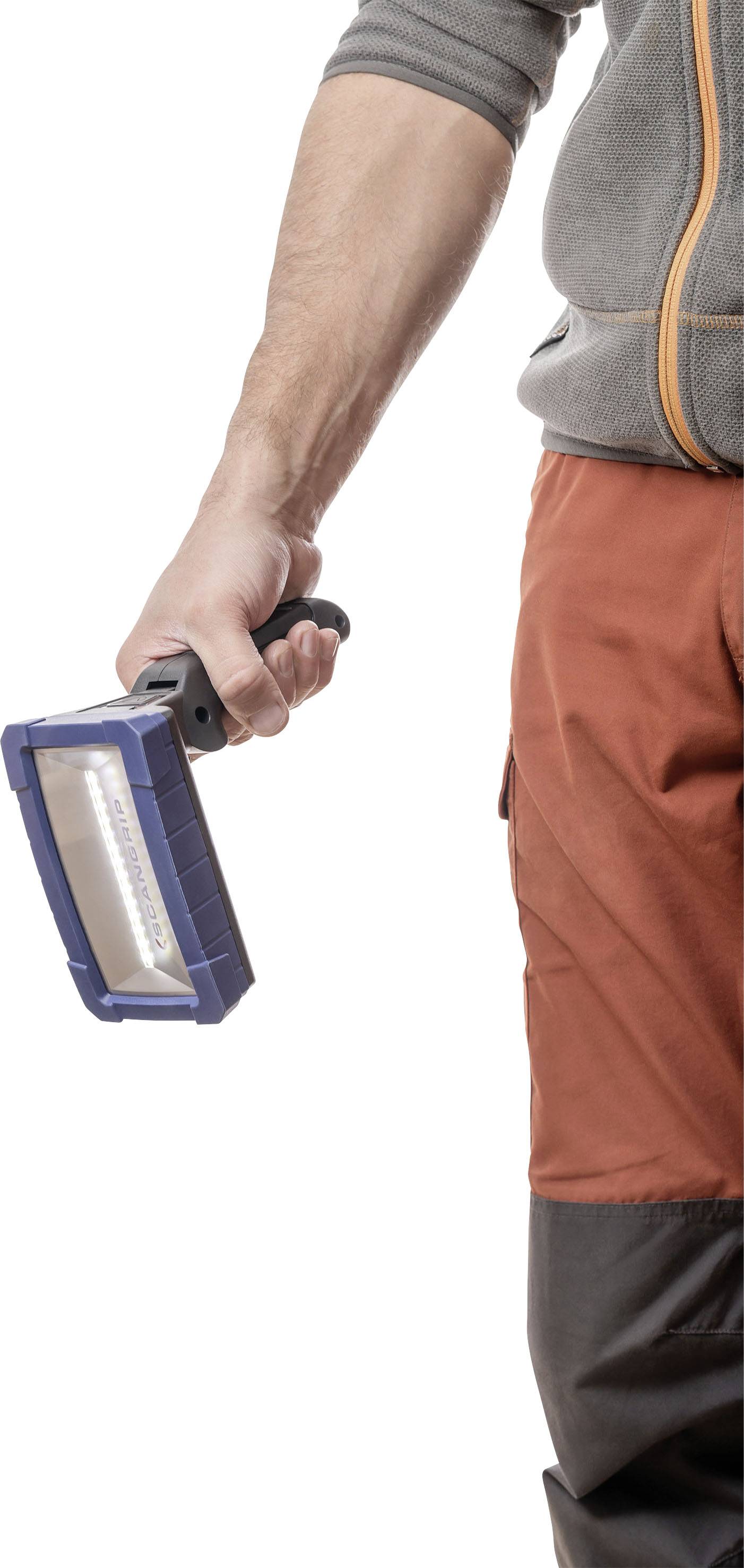 Osoba trzyma niebieską przenośną lampę w prawej ręce na neutralnym tle.