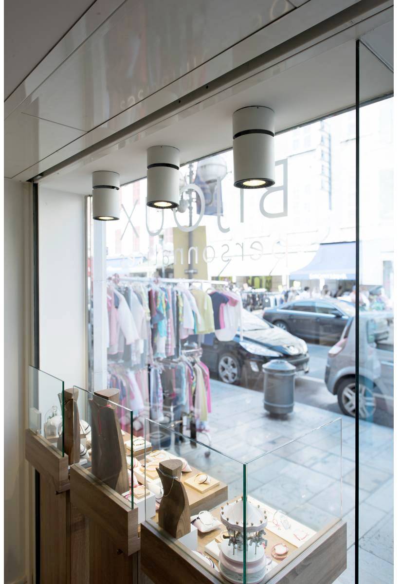 Witryna sklepowa jubilera prezentująca różne wyroby biżuteryjne. W tle widoczne są wieszaki z odzieżą oraz przejeżdżające samochody.