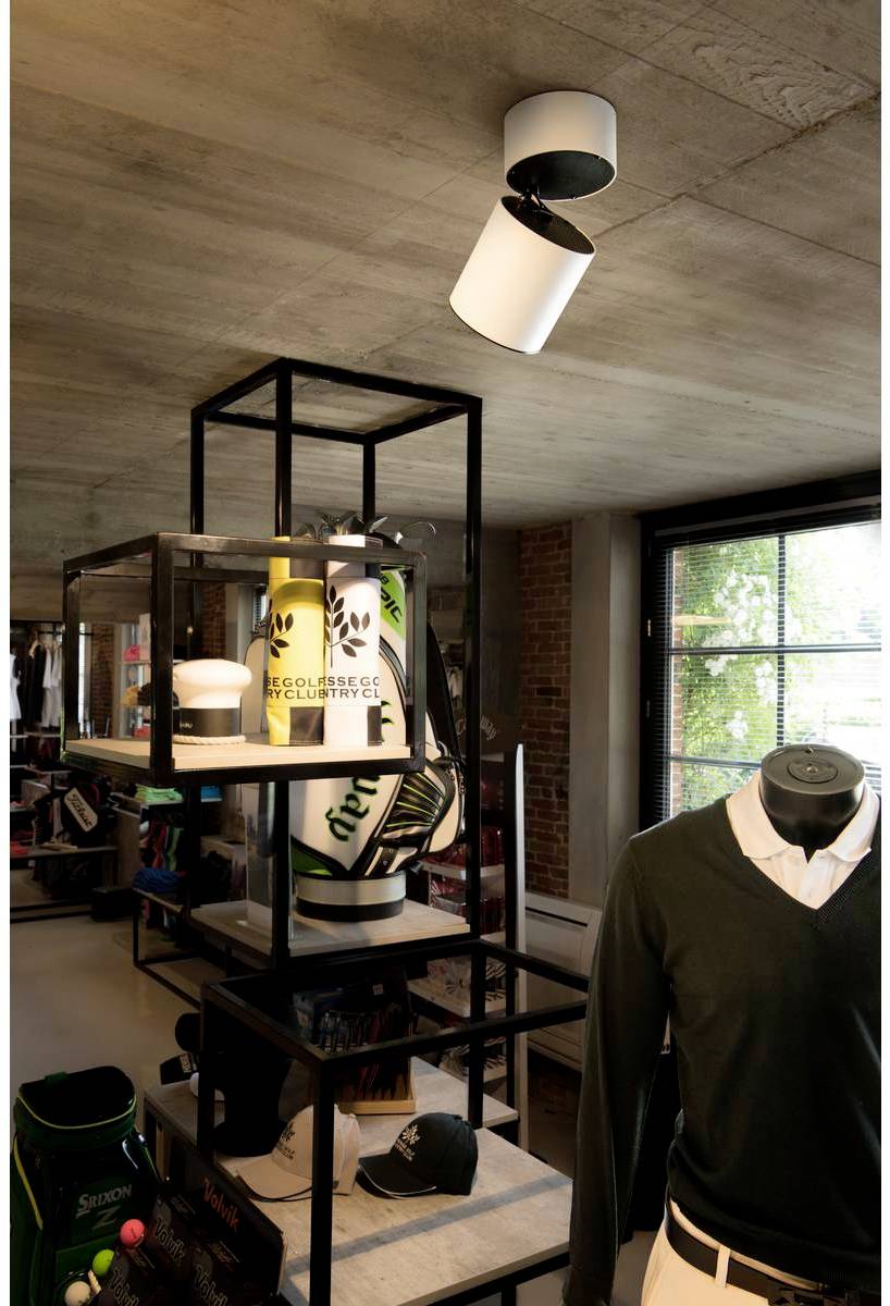 Nowoczesny sklep z odzieżą golfową i akcesoriami. Manekin prezentuje zieloną koszulkę polo. W tle widać półki z wyposażeniem golfowym.