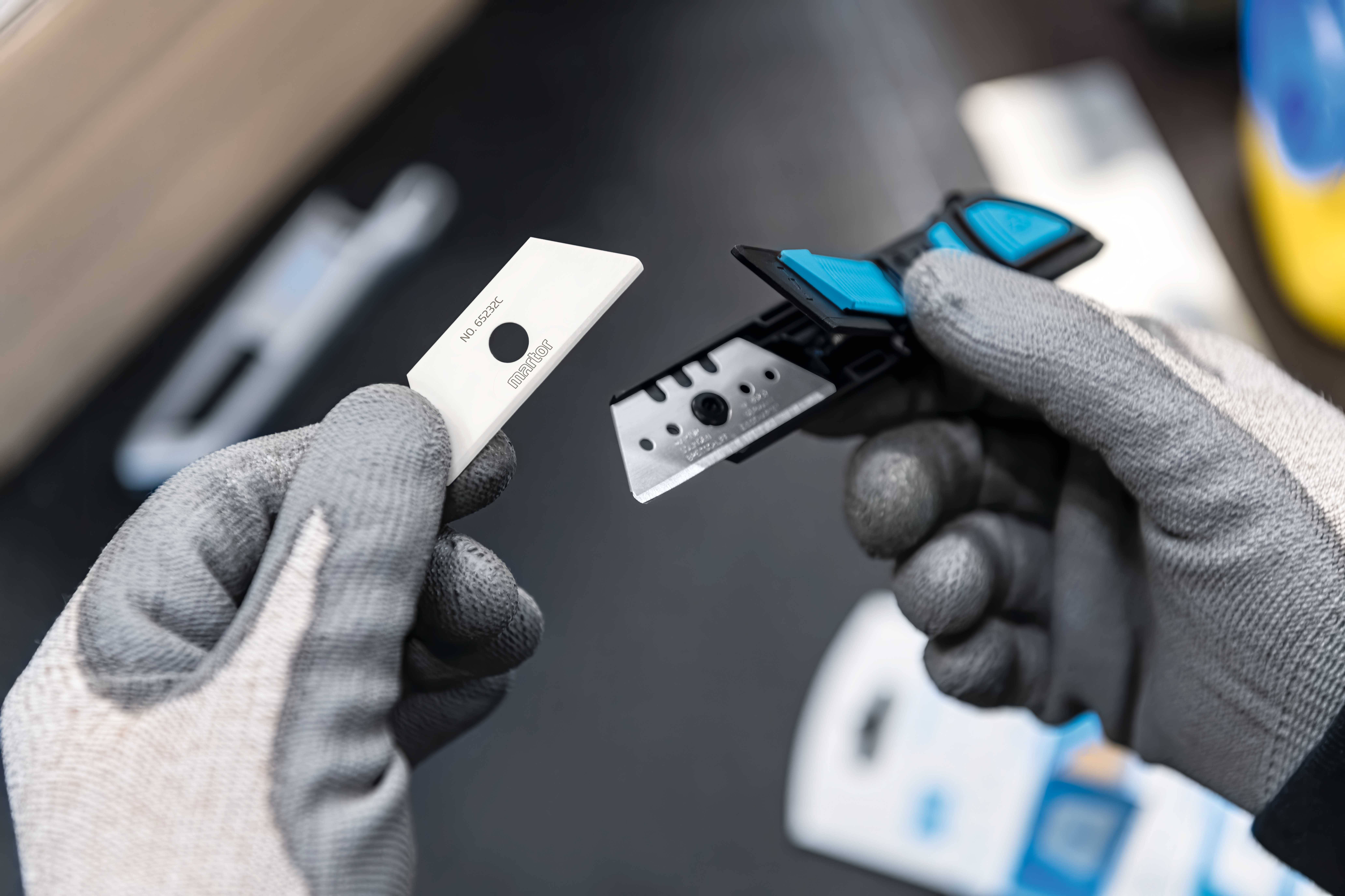 Osoba w szarych rękawiczkach trzyma dwie różne ostrza do golenia w rękach, przygotowując się do wymiany ostrza.