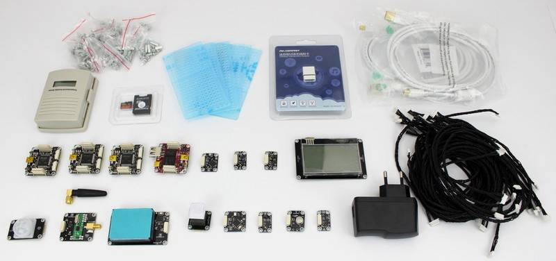 Różnorodne elementy elektroniczne, w tym liczne czujniki, płytki drukowane, przewody i akcesoria, ułożone na białym tle.