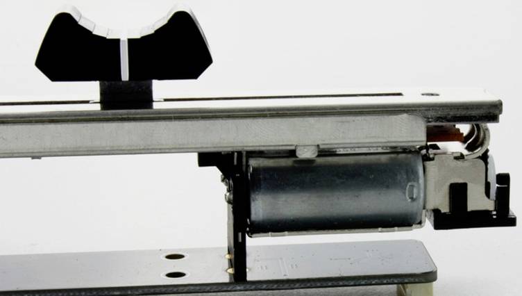 Zbliżenie mechanicznego urządzenia z silnikiem elektrycznym i mechanizmem dźwigniowym na metalowej podstawie na białym tle.