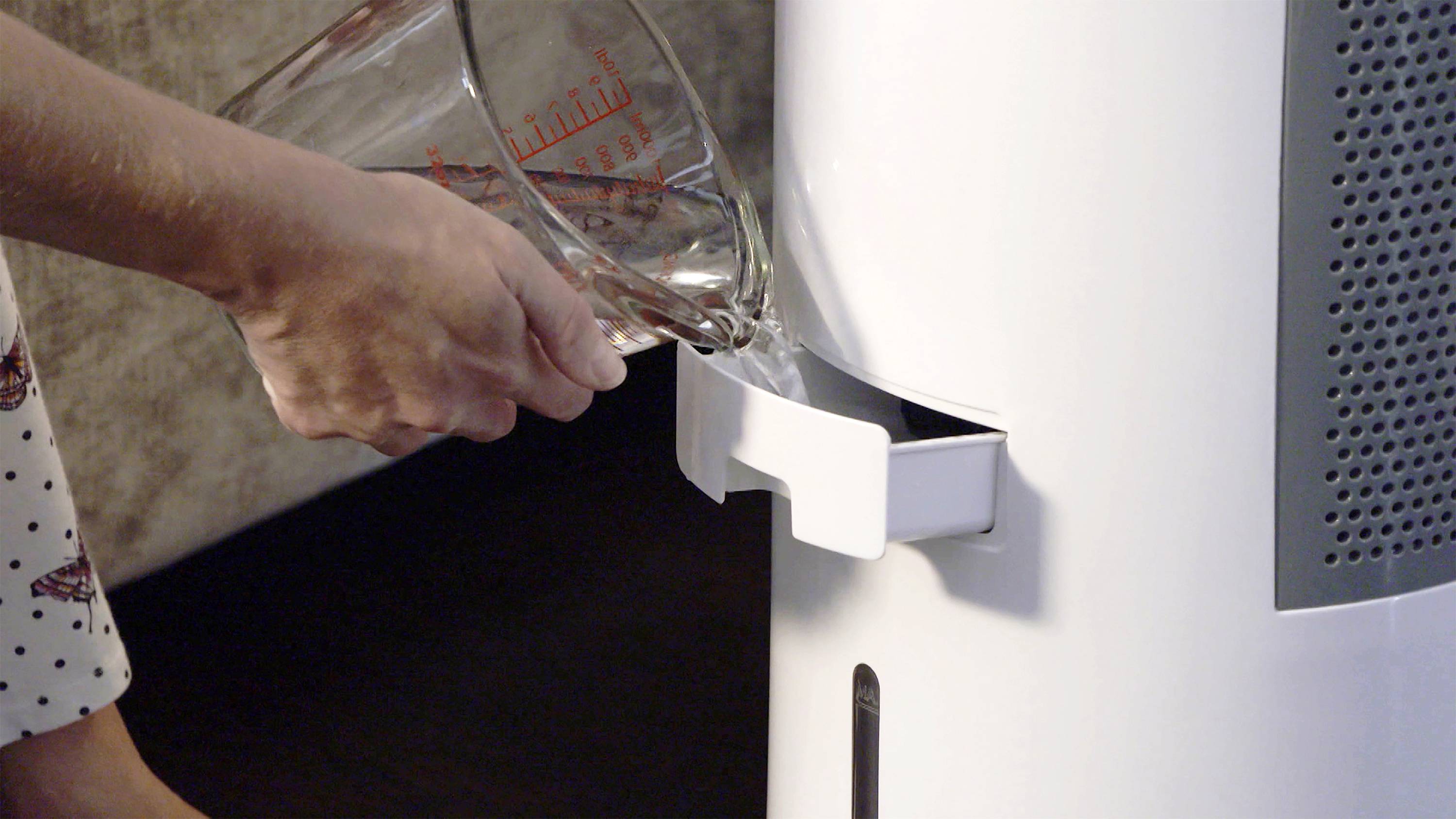 Osoba nalewa wodę z miarki do białego nawilżacza powietrza.