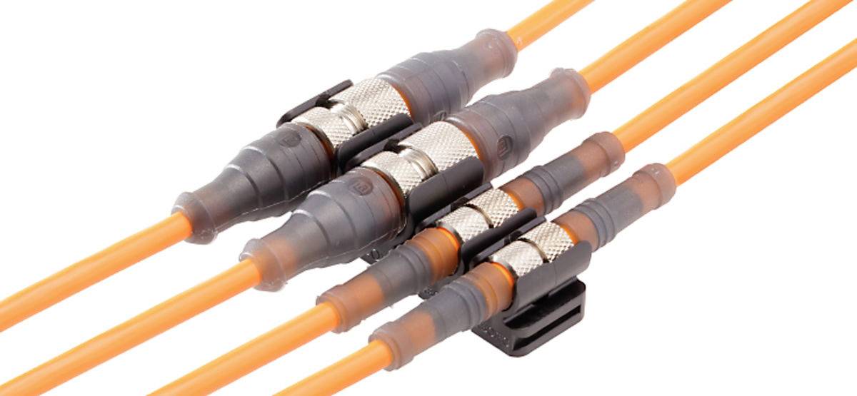 Cztery pomarańczowe kable światłowodowe z czarnymi i srebrnymi złączami biegną równolegle.