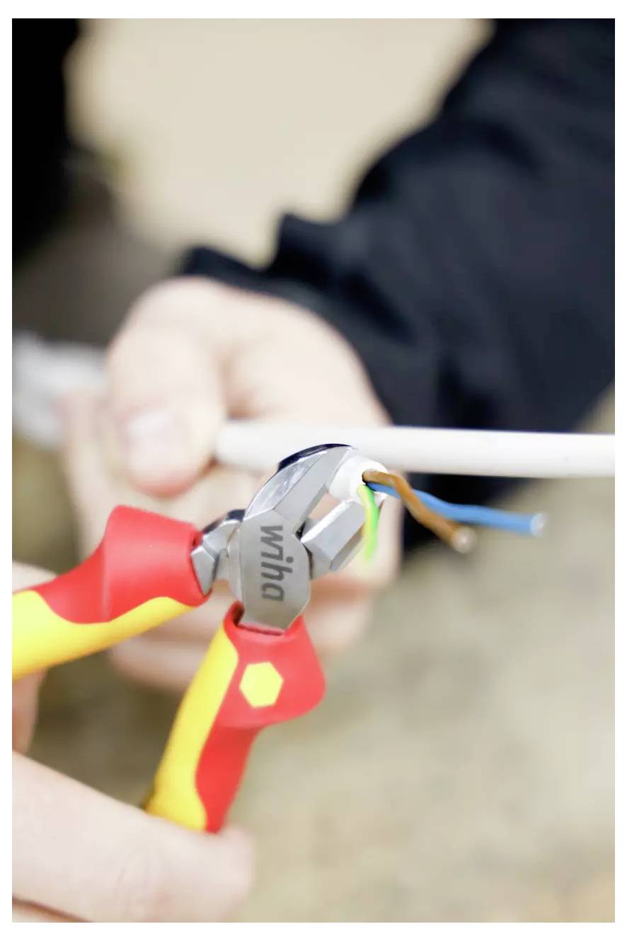 Dłonie używające obcinaczy drutu do rozłupywania przewodu elektrycznego, odsłaniające kolorowe przewody wewnętrzne.