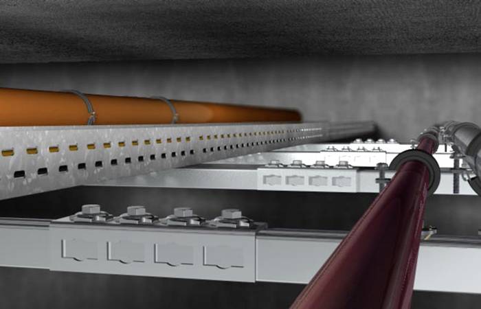 Instalacja kabli w tunelu. Metalowe uchwyty mocno przytwierdzają pomarańczowe i czerwone kable do sufitu i ściany.