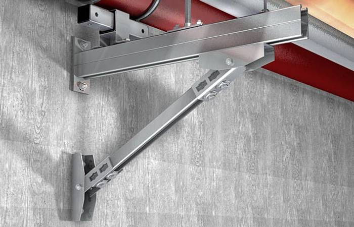 'Metalowy nośnik zamontowany na ścianie, czerwona rura na górze, szara powierzchnia ściany. Przemysłowa instalacja infrastruktury.'