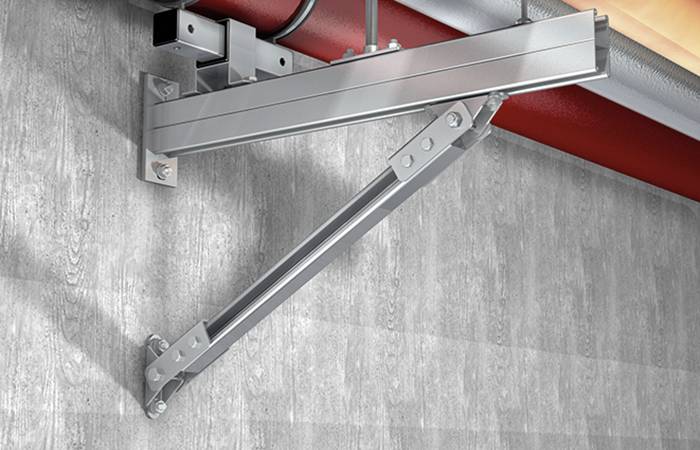 Stalowa konstrukcja do mocowania rur na ścianie, prezentująca stabilny uchwyt z wieloma śrubami zamocowanymi w ścianie betonowej.