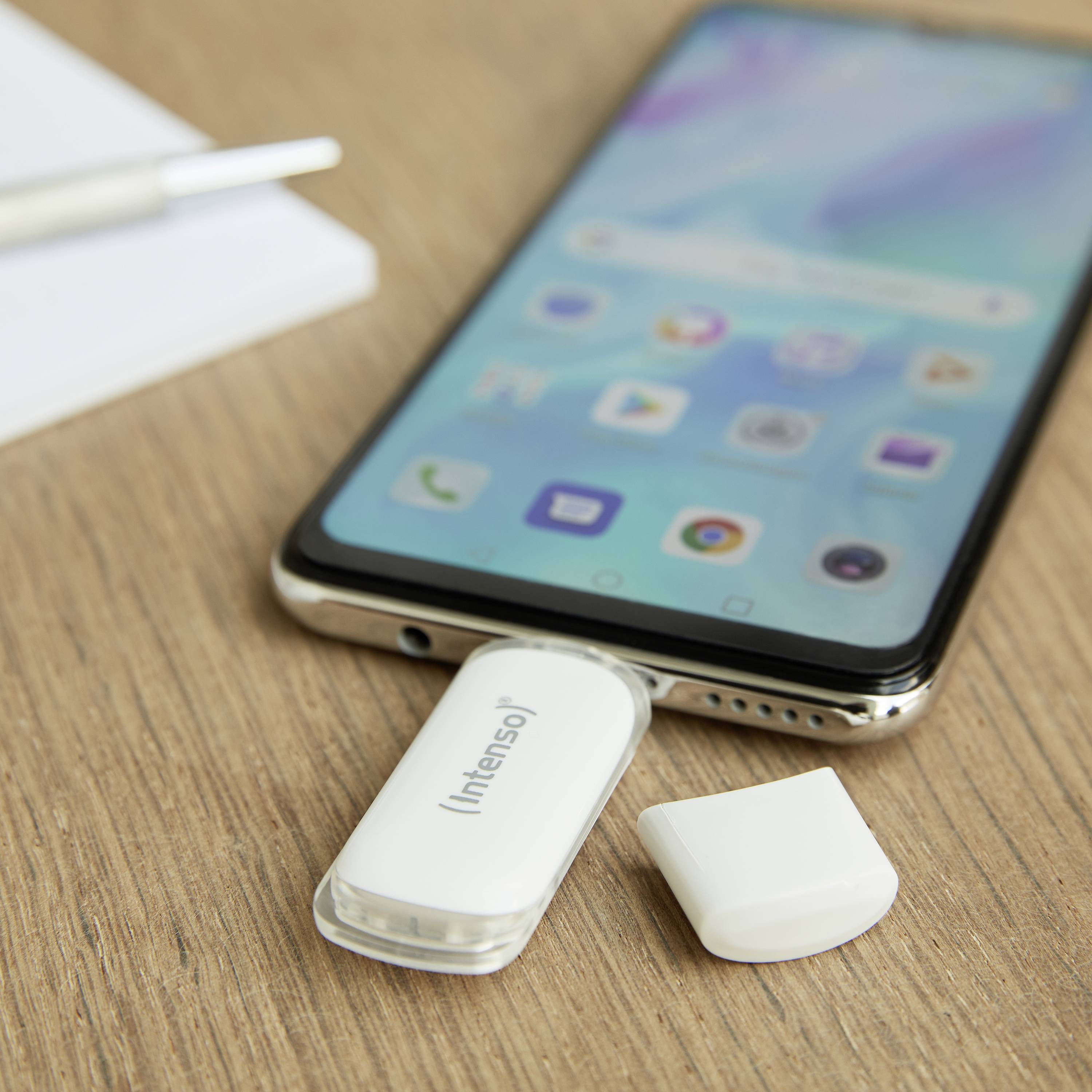 Smartfon leży na stole. Pendrive jest włożony do smartfona. Obok niego znajduje się zdjęty nasadka.