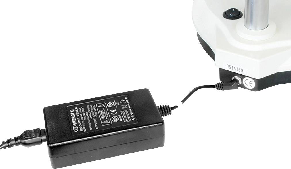 Czarny zasilacz podłącza się do urządzenia elektrycznego. Na zasilaczu widoczne są specyfikacje techniczne.