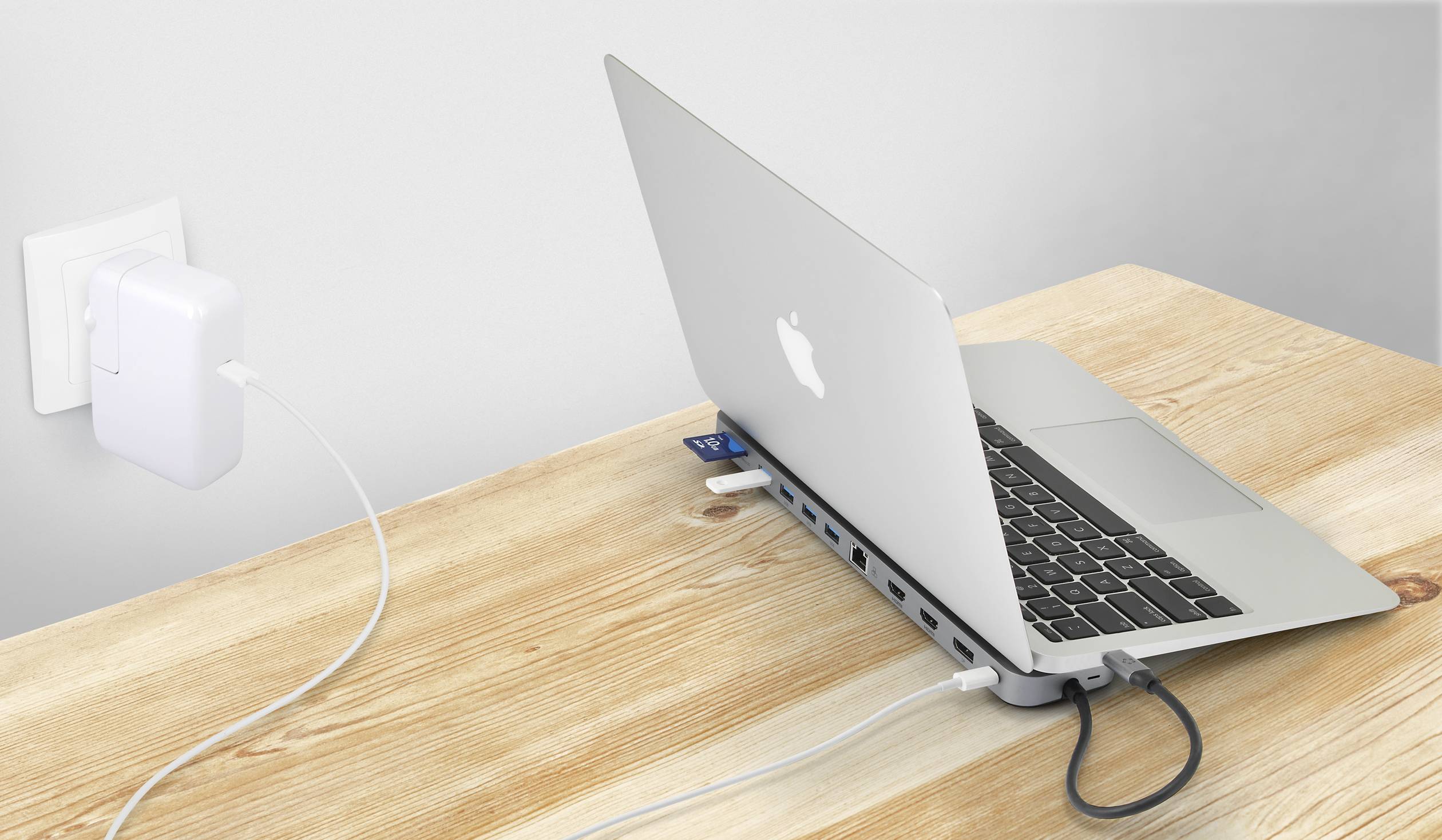 Srebrny laptop jest podłączony do rozgałęziacza USB z wieloma kablami i portami, znajdujący się na drewnianym stole.