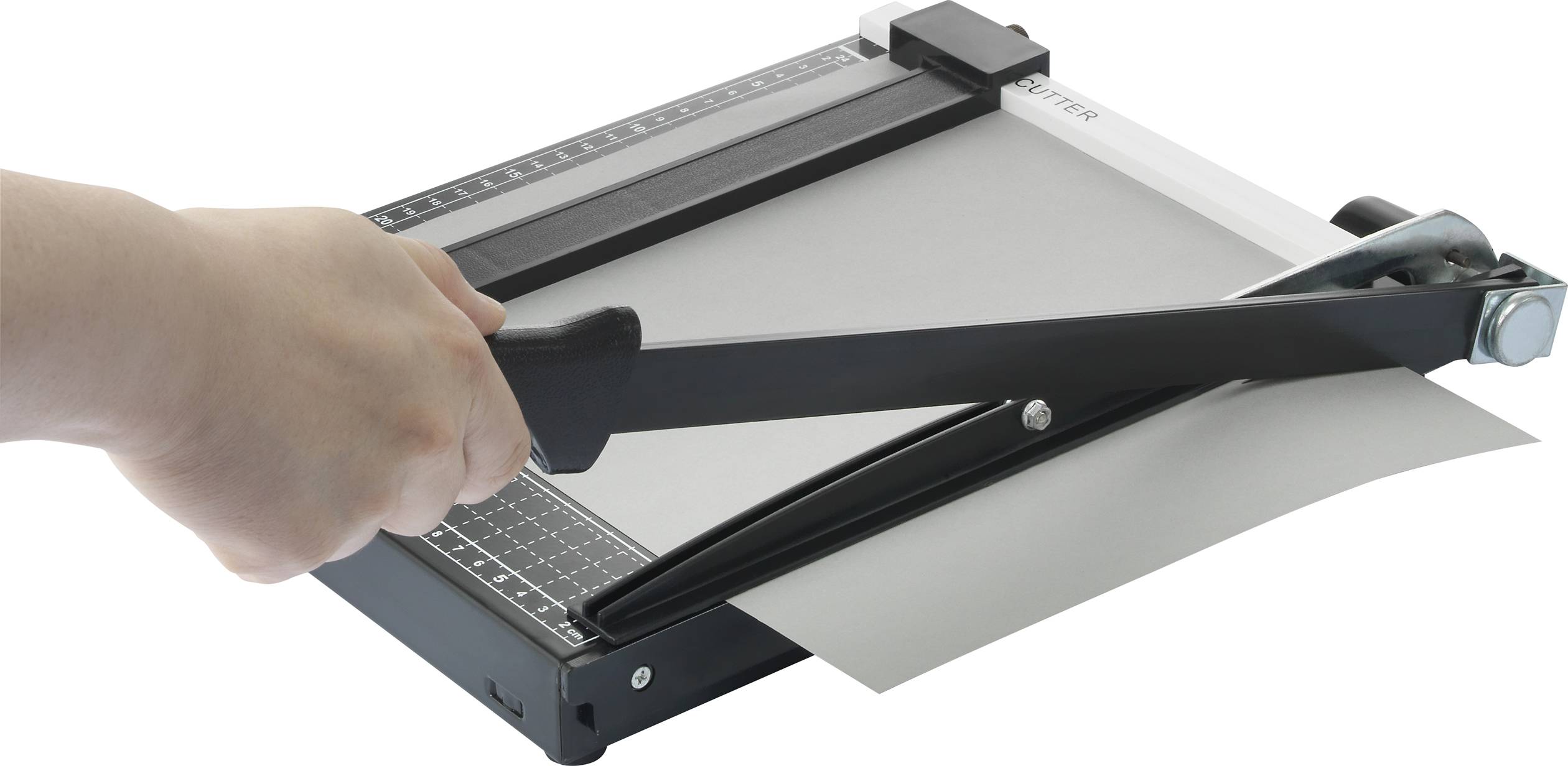 Jedna ręka kroi kartkę papieru trymerem na stole. Trymer posiada linijki do precyzyjnego pozycjonowania.