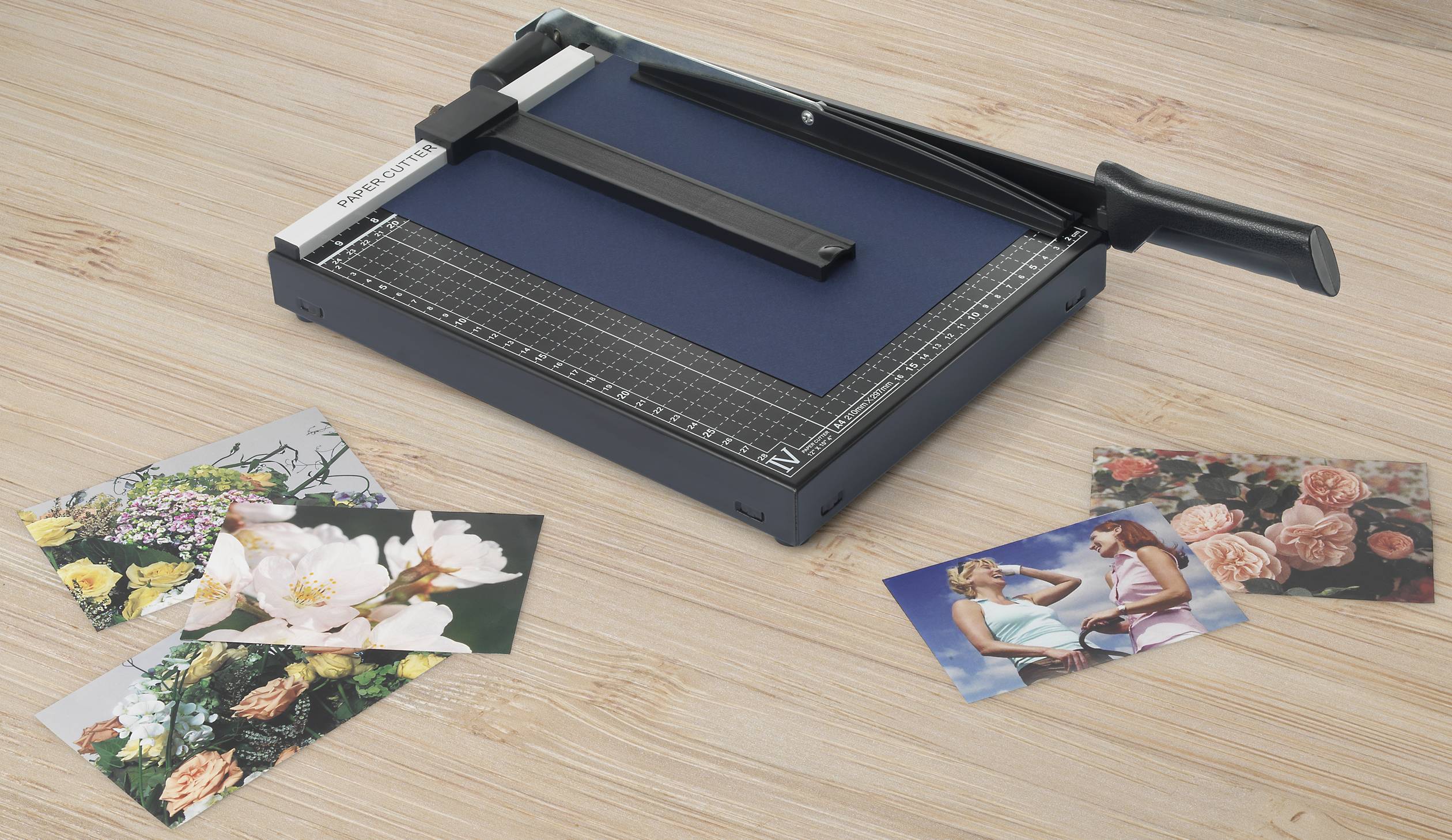 Krajarka do papieru na drewnianym stole z kilkoma kolorowymi zdjęciami kwiatów i osób.