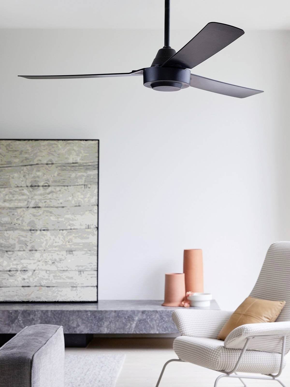 Salon z nowoczesnym wentylatorem sufitowym, szarą sofą, białym fotelem z poduszką oraz dwoma pomarańczowymi wazonami.