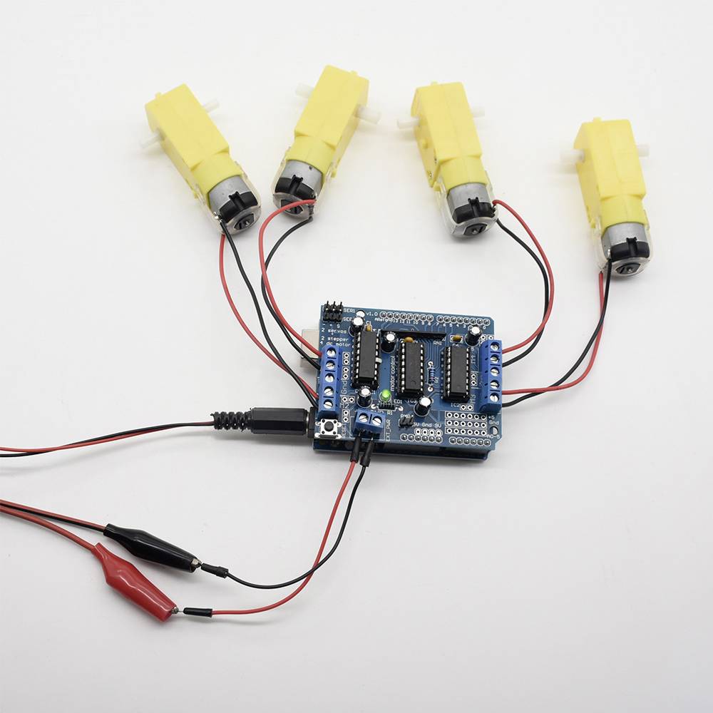 Niebieska płytka drukowana jest połączona z czterema żółtymi silnikami oraz czerwonymi i czarnymi przewodami. Płytka świeci zielonymi diodami LED.