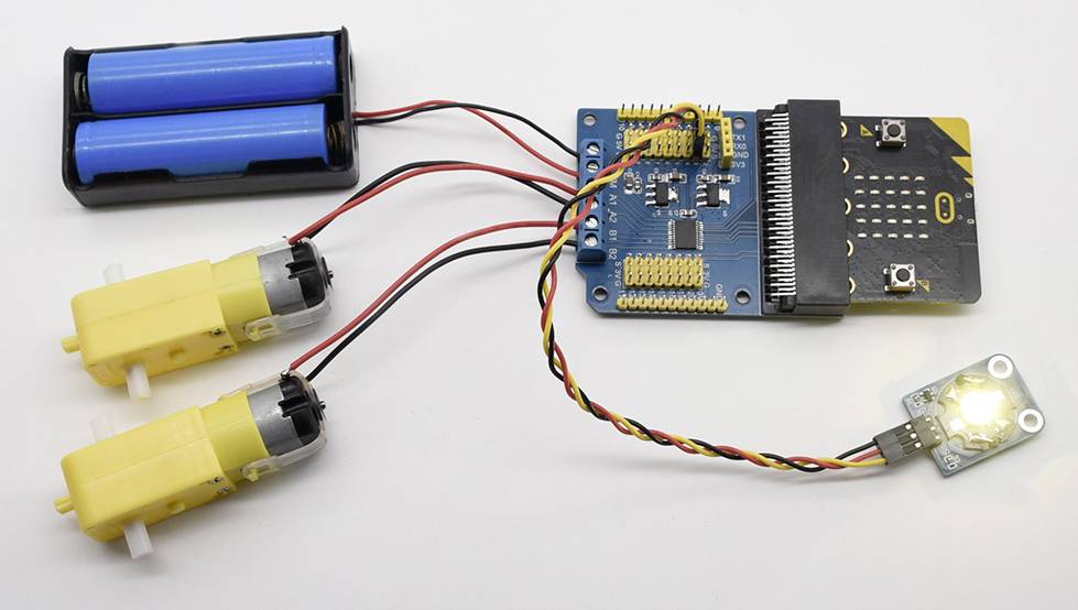 Prosty obwód elektryczny z mikrokontrolerem, dwoma żółtymi silnikami, uchwytem na dwie baterie i świecącą diodą LED.