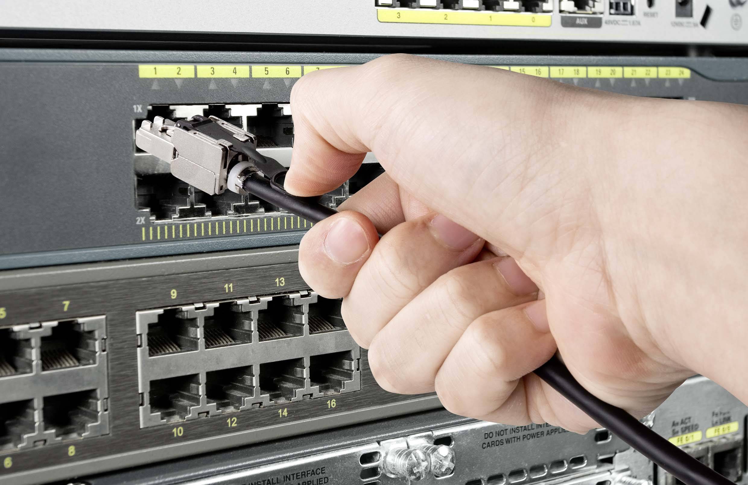 Ręka wkłada kabel do przełącznika sieciowego, co wskazuje na połączenie lub konfigurację sieci.