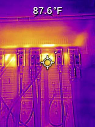 Termowizyjne zdjęcie szafy elektrycznej pokazuje przegrzanie przy 87,6°F, sygnalizowane ciepłymi kolorami w górnej części na kilku styках.