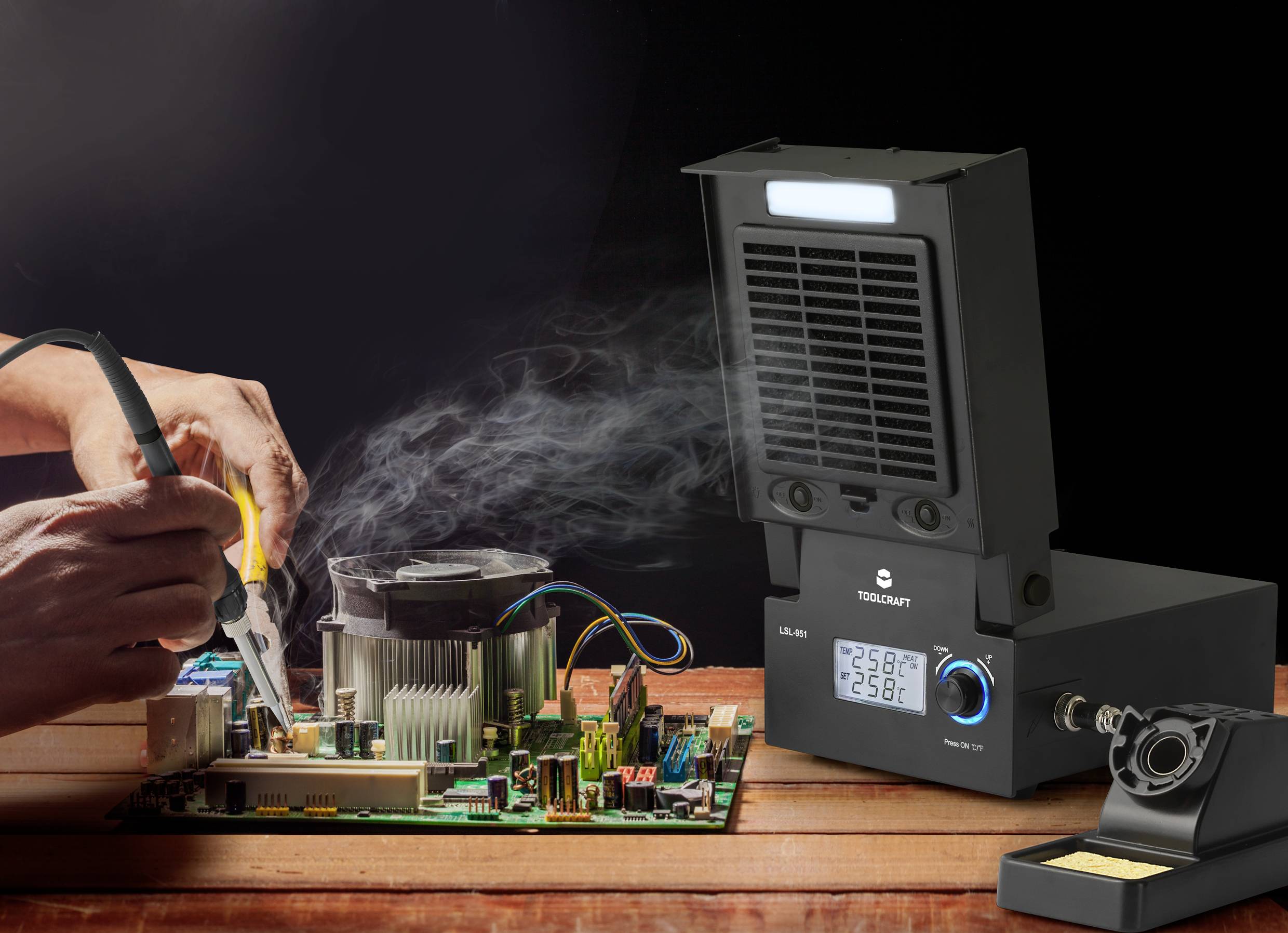 Osoba lutuje na płytce drukowanej, podczas gdy unosi się dym. Obok czarny lutownik z wyświetlaczem cyfrowym na drewnianym stole.