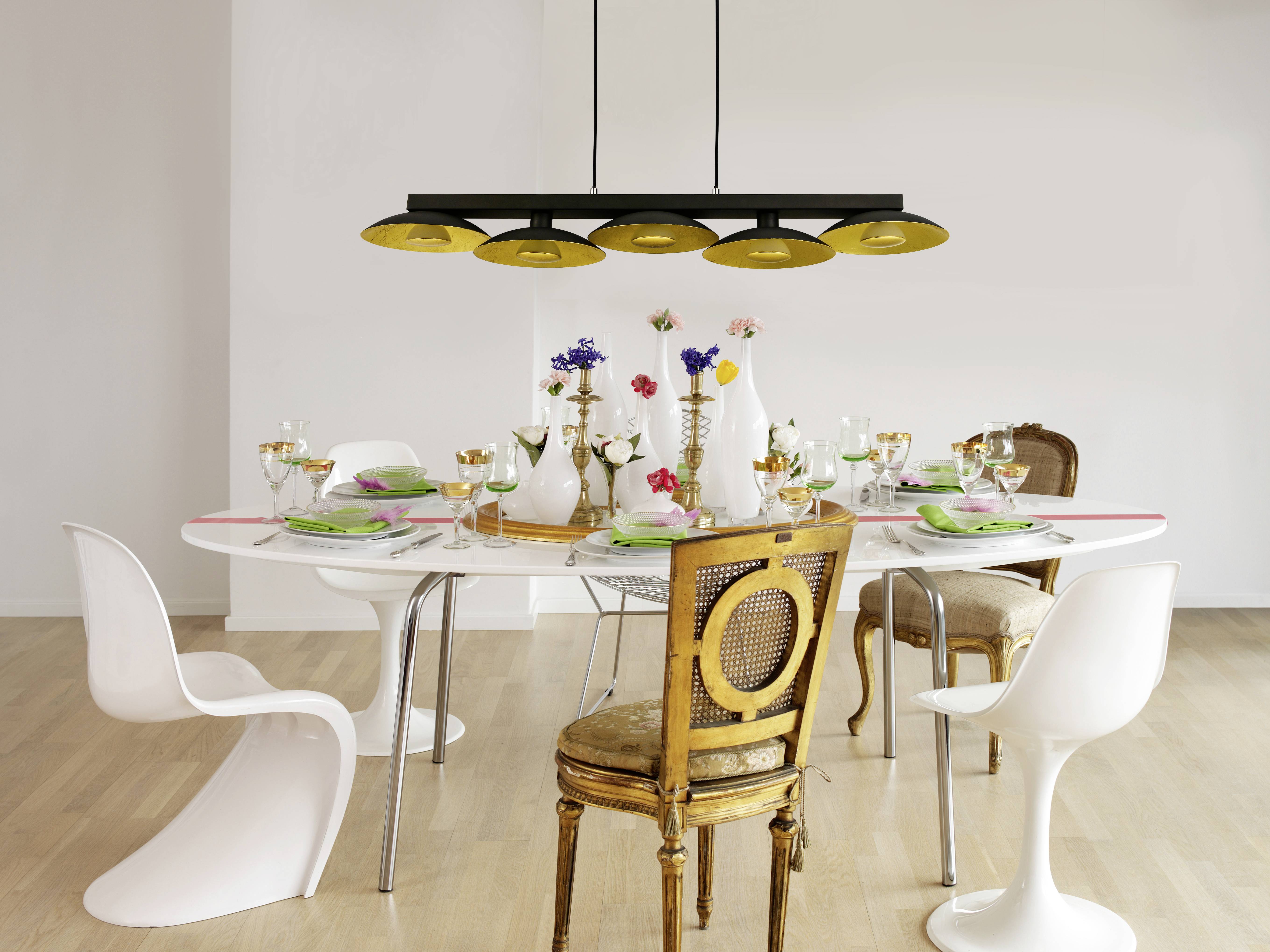 Elegancko nakryty stół jadalny z białymi i brązowymi krzesłami, ozdobiony wazonami z kwiatami, zastawą stołową i kieliszkami pod nowoczesną lampą.