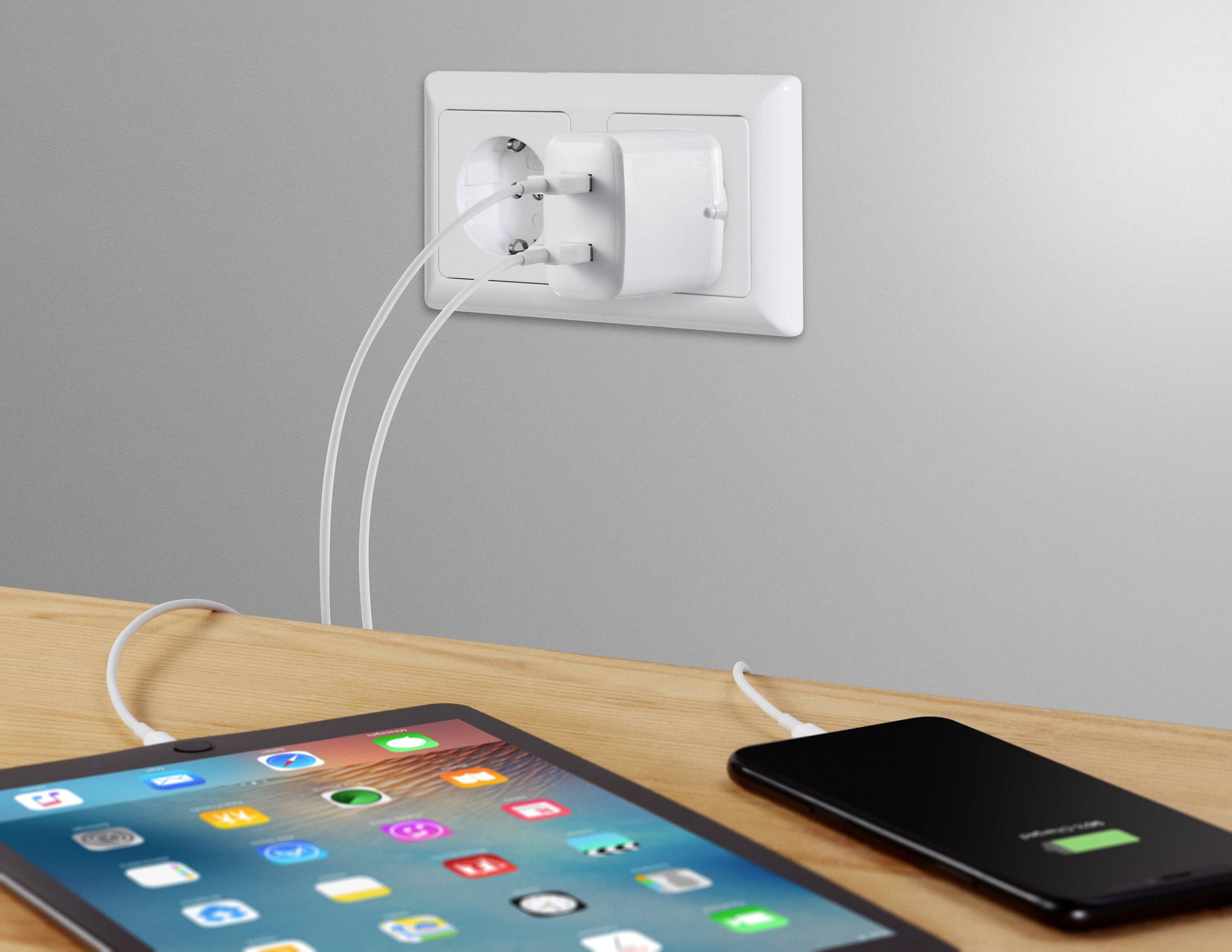 Tablet i smartfon są ładowane przez podwójną ładowarkę w jednym gnieździe elektrycznym, oba wyświetlają symbole ładowania.