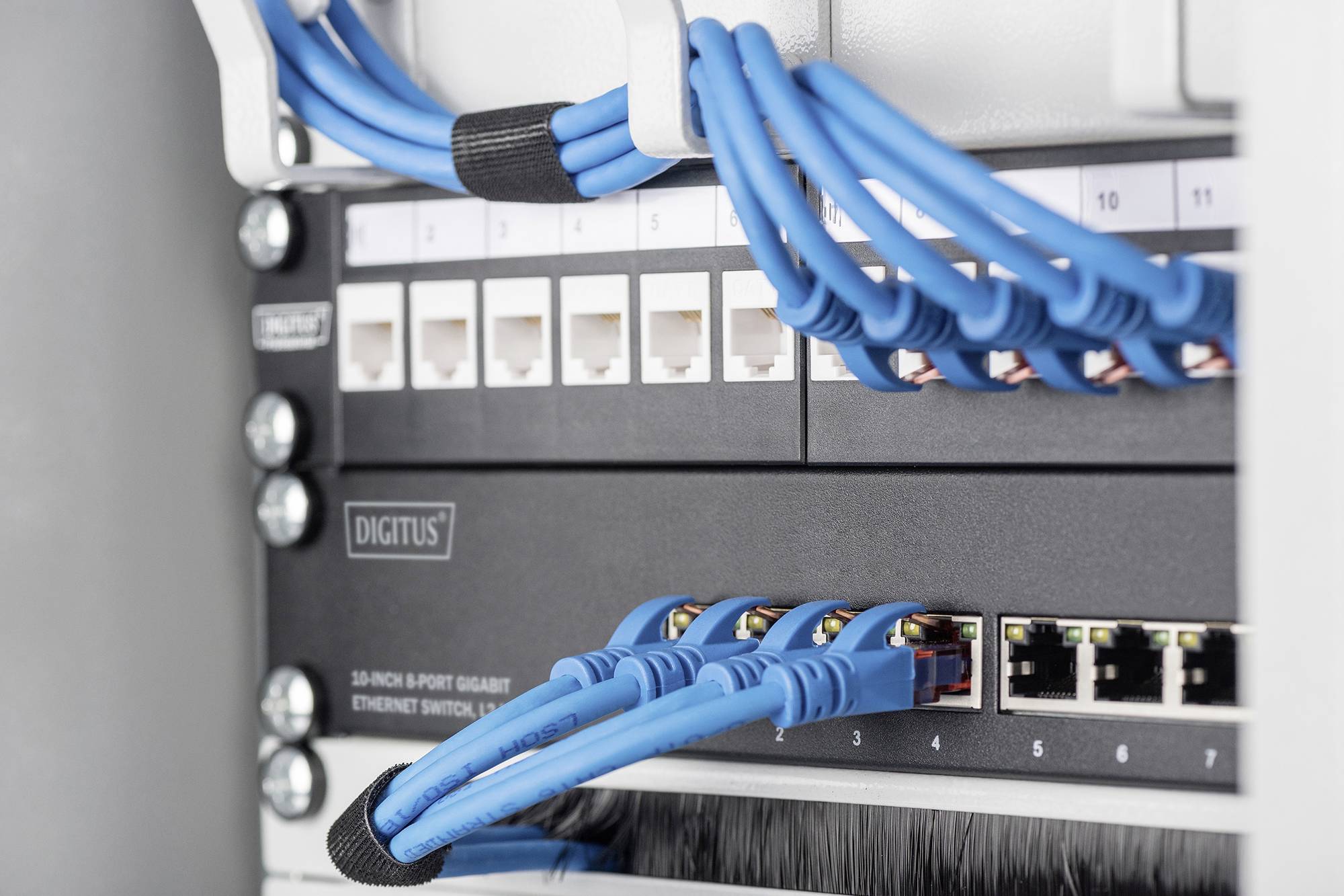 Przełącznik sieciowy w serwerowni z ośmioma podłączonymi niebieskim kablami Ethernet i ponumerowanymi portami.