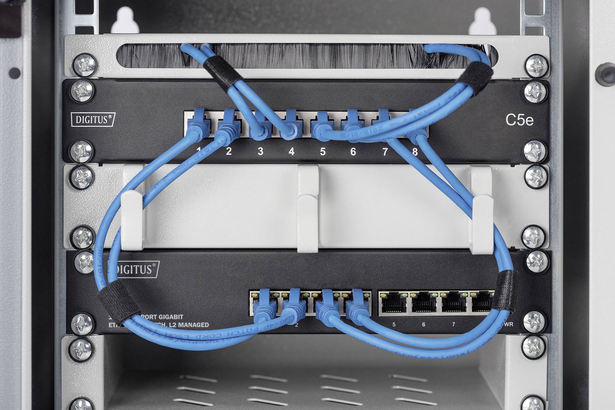 Szafa dystrybucyjna sieciowa z niebieskimi kablami Ethernet podłączonymi do patch panela i switcha.