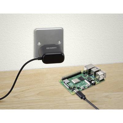 Raspberry Pi widoczny jest na drewnianym stole, podłączony do zasilacza włożonego do gniazdka elektrycznego.