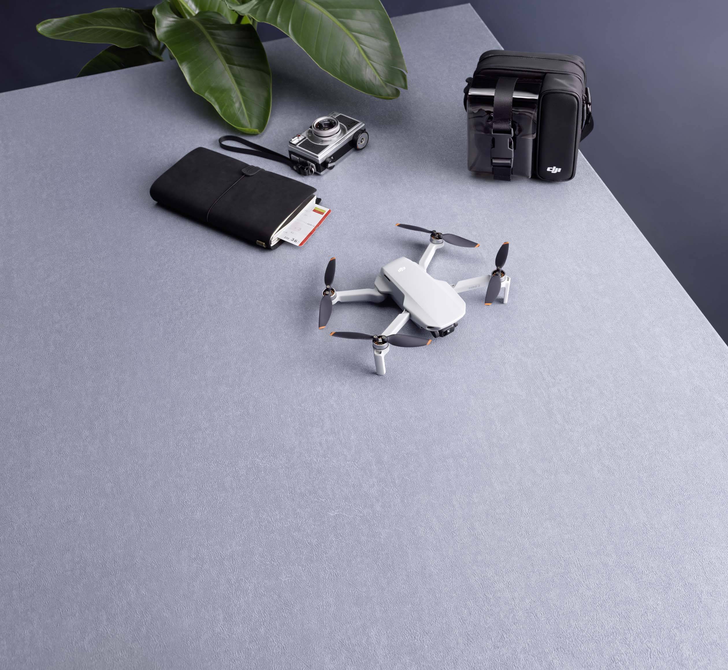 Na stole leży biały dron obok kompaktowego aparatu fotograficznego, czarnej torby i czarnego etui.