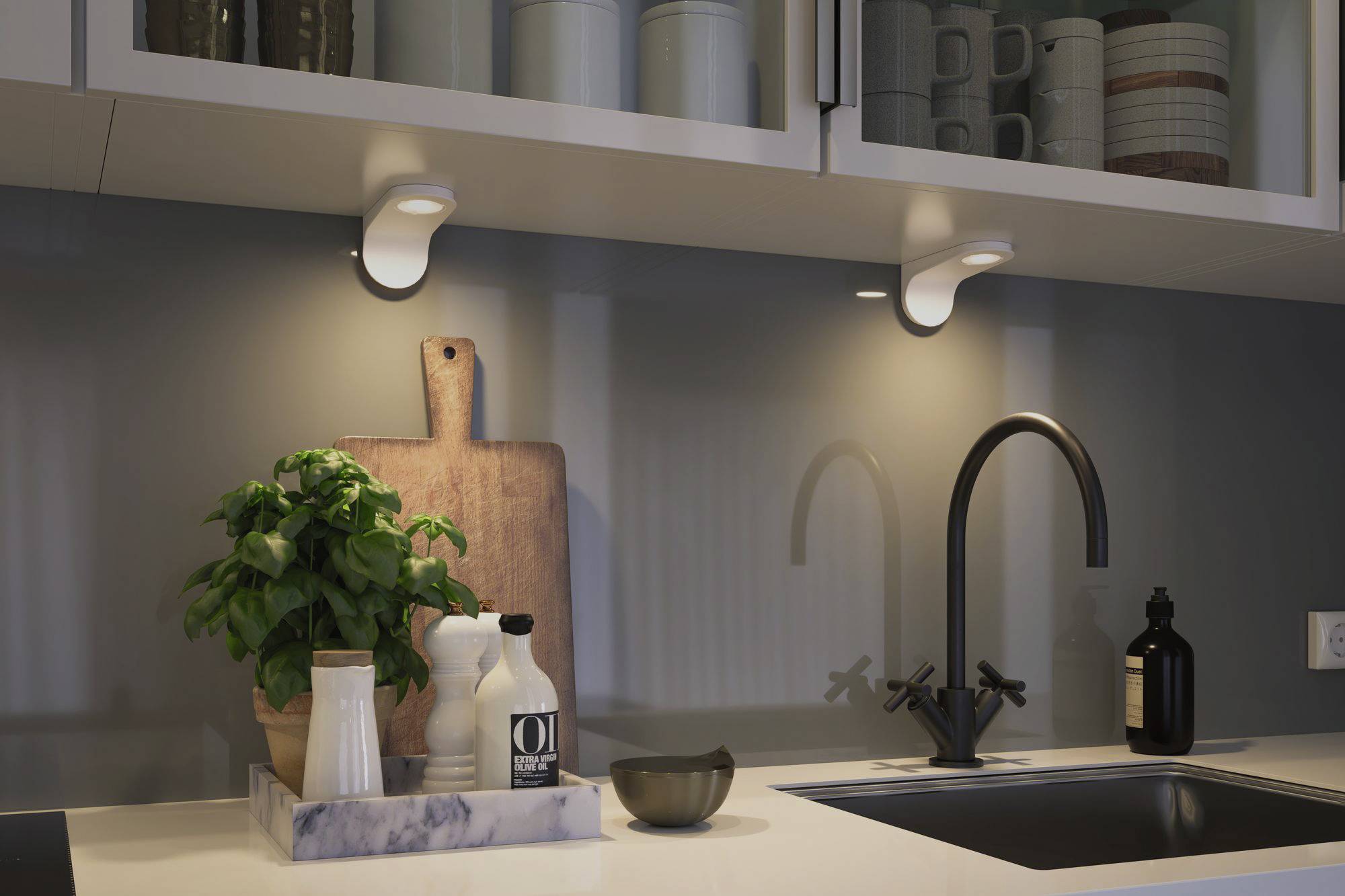 Nowoczesna kuchnia z białym blatem, czarnym zlewem, pod spodem deska do krojenia, solniczka i pieprzniczka oraz roślina bazylii.