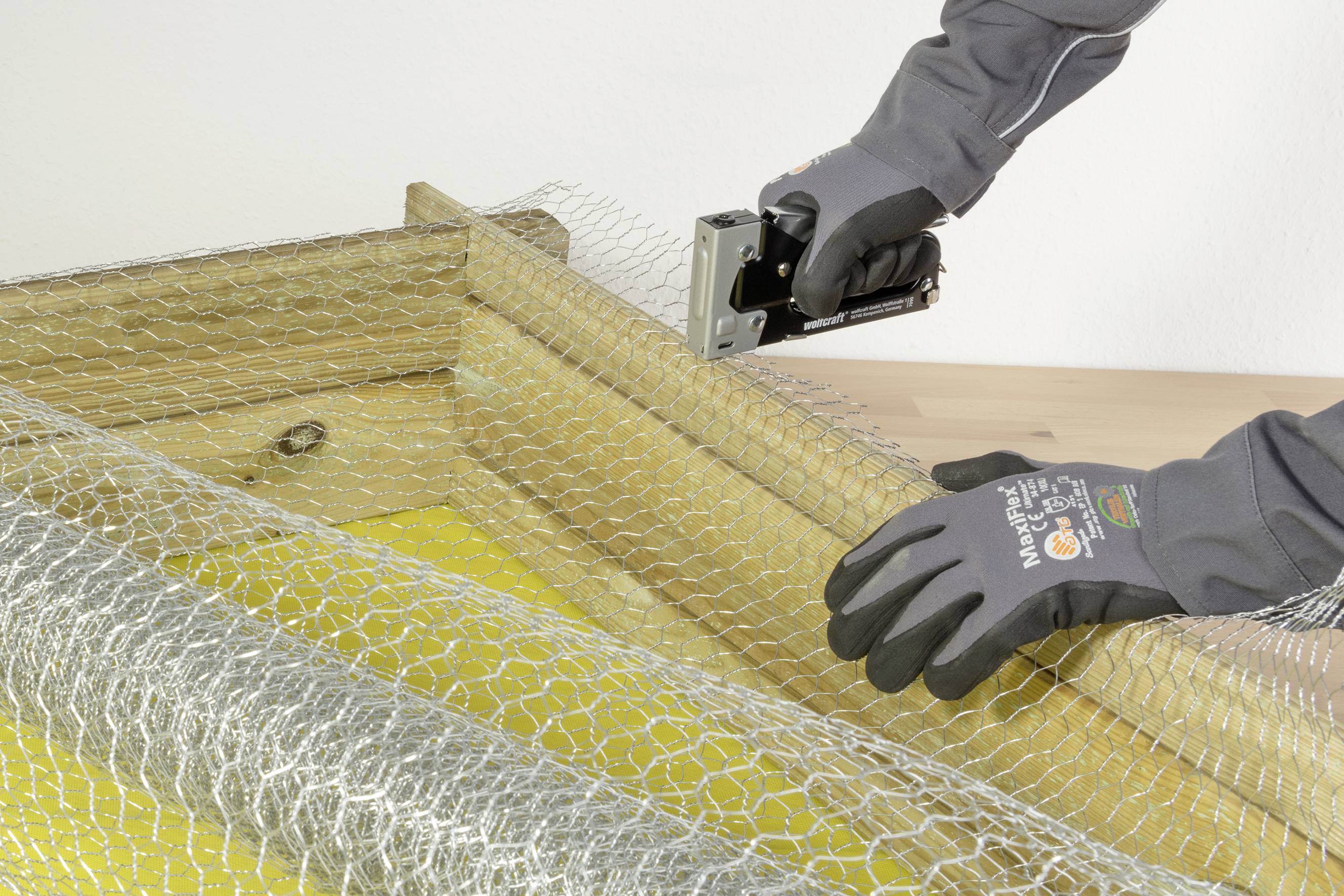 'Osoba mocuje siatkę ogrodzeniową zszywkami do drewnianej ramy.'